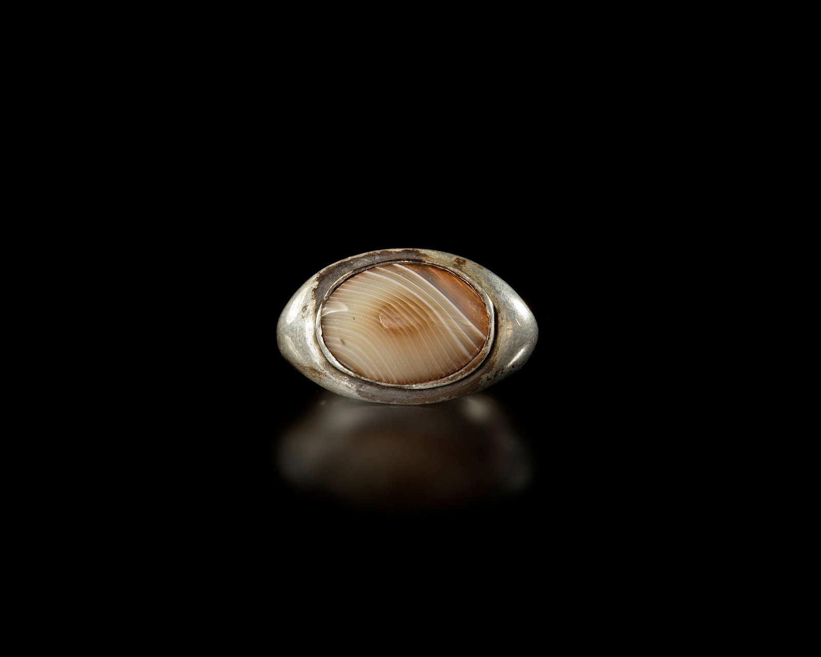 A SILVER RING WITH AGATE, 19TH CENTURY: A solid silver ring set with a polished oval agate displaying natural concentric banding in warm earthy tones. Stone 17 by 13 mm. EU size 60, US size 9