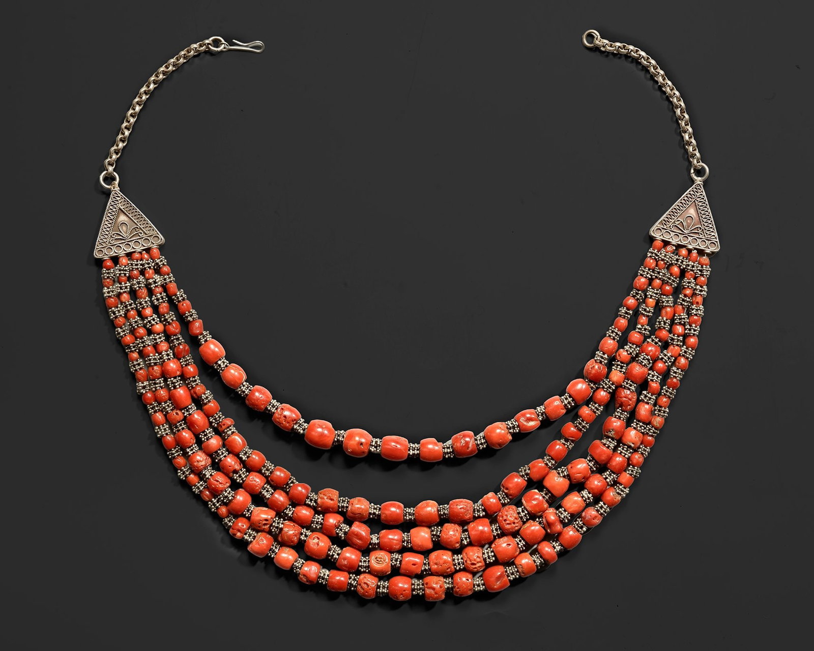 A SILVER AND CORAL NECKLACE,YEMEN, 19TH CENTURY: A Yemeni necklace composed of multiple strands of vibrant coral beads linked with small silver elements and finished with triangular silver plaques. The cascading beadwork creates a broad decorative f