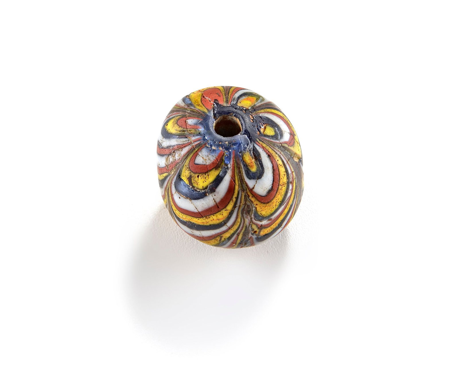 A VENETIAN COMBED MILLEFIORI GLASS BEAD,19TH CENTURY: A bold Venetian glass bead with hand-combed feathered patterns. Deep cobalt blue base layered with bright canary yellow, brick red, and white glass canes, pulled into sharp V-shaped feathers. The surf