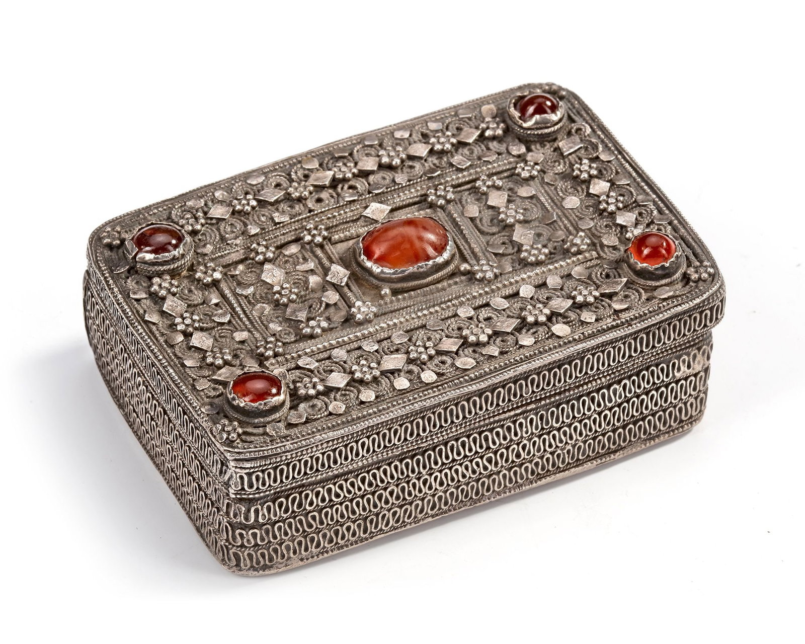 A SILVER BOX, YEMEN, 19TH CENTURY: Richly decorated with intricate filigree, granulation, and geometric motifs. The lid is set with five polished red stones, including a larger central cabochon, framed by detailed silver work. 8 by 6 c