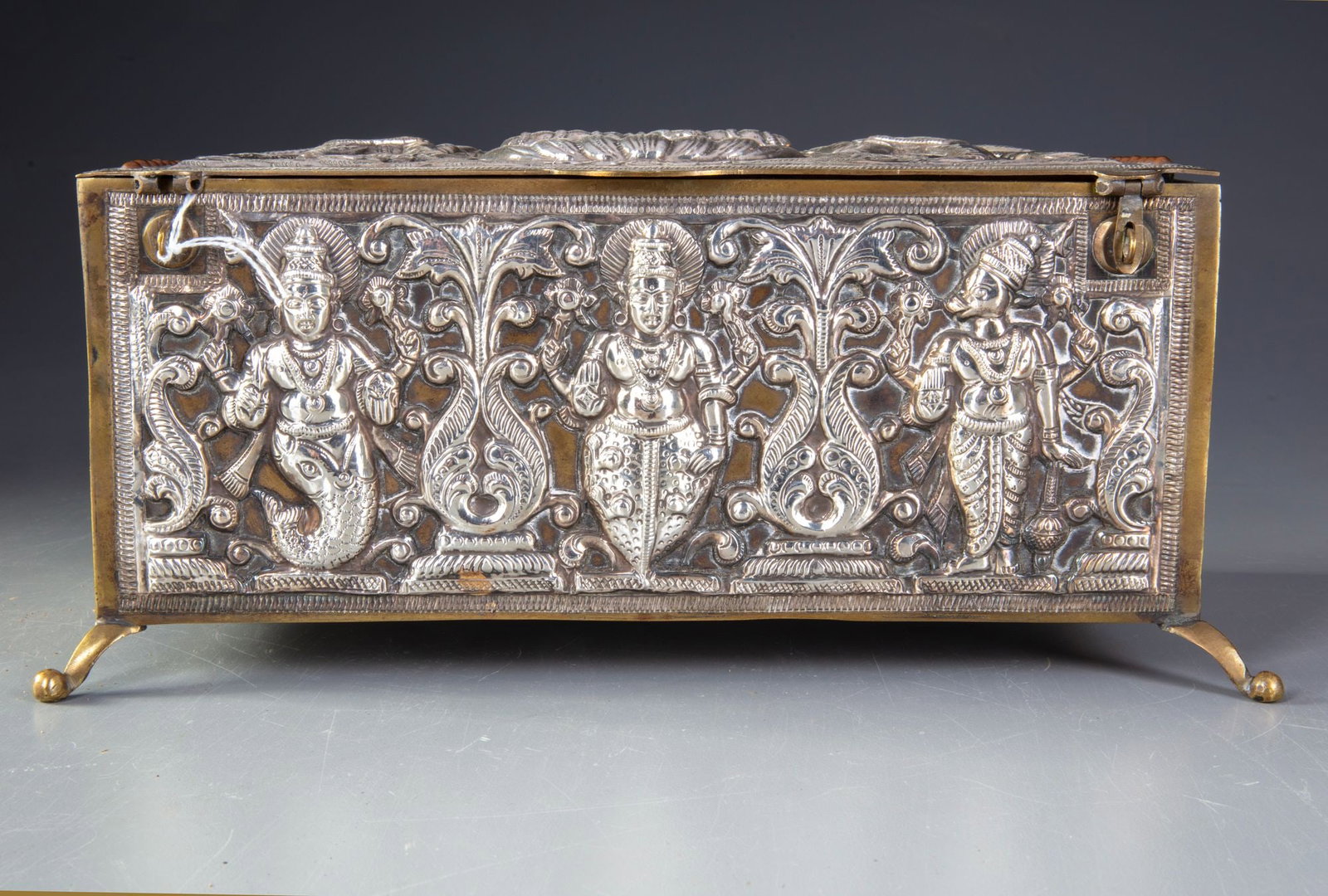 AN ISLAMIC SILVER ELONGATED BOX, INDIA, 19TH CENTURY: Richly decorated in high relief with intricate repouss?© work. The panels feature detailed depictions of deities, mythological figures, and ornate floral scrolls framed within architectural borders. 