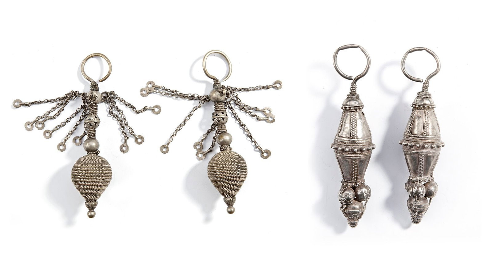 TWO PAIR OF SILVER EARRINGS, YEMEN, 19TH CENTURY: A rare set of four Yemeni silver earrings from the 19th century, each pair showcasing distinct traditional designs. Two feature large granulated drop pendants with chain tassels, while the other pair 