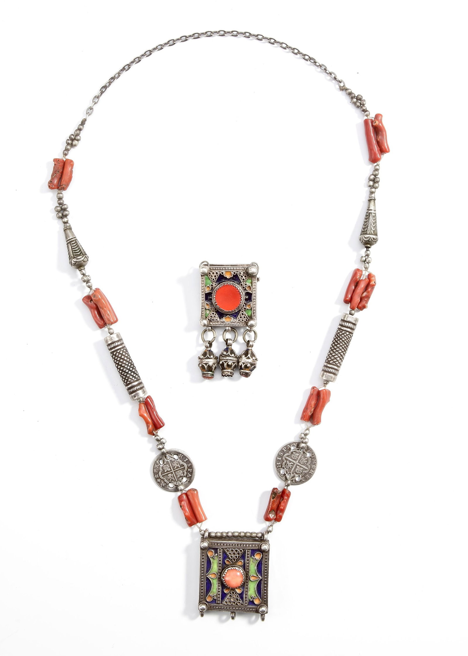 AN ISLAMIC SILVER NECKLACE, MOROCCO, 19TH CENTURY: Decorated with coral beads, enamel panels, and Spanish silver coins. The central pendants feature brightly colored enamel in green, blue, and orange surrounding cabochon stones, symbolizing protection