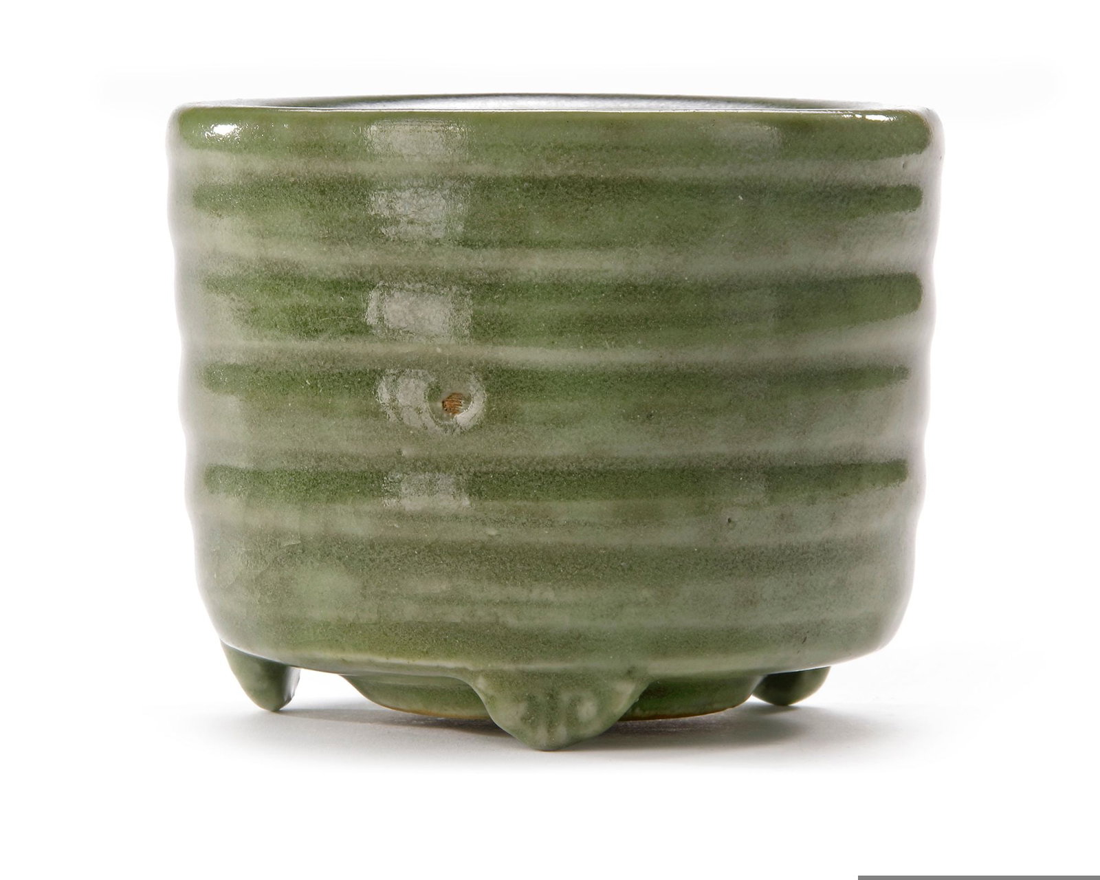 A CHINESE LONGQUAN TRIPOD INCENSE BURNER, YUAN/MING DYNASTY (14TH-15TH CENTURY): A Chinese tripod incense burner with grey green glaze inside and outside. The body with five carved horizontal lines. The base unglazed and burnt red in the firing. Height: 7.3 cm. Diameter: 9.4 cm. A