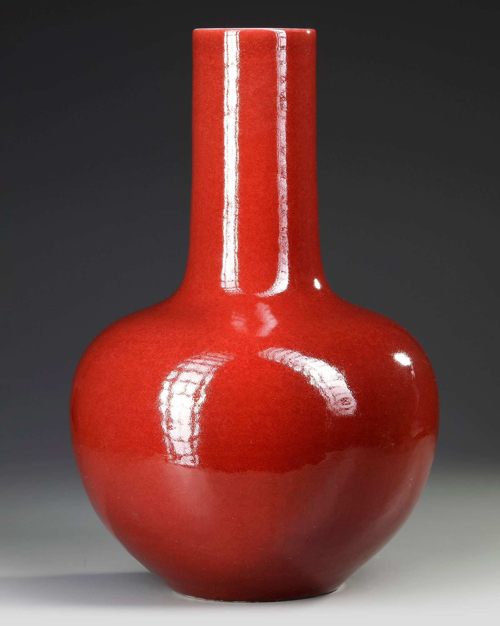 A LARGE CHINESE RED GLAZED BOTTLE VASE, 19TH-20TH CENTURY: The vase is shaped with a globular body and a cylindrical neck. It is covered with a strawberry-red glaze thinning slightly at the rim and stopping neatly at the foot. Height 51 cm.