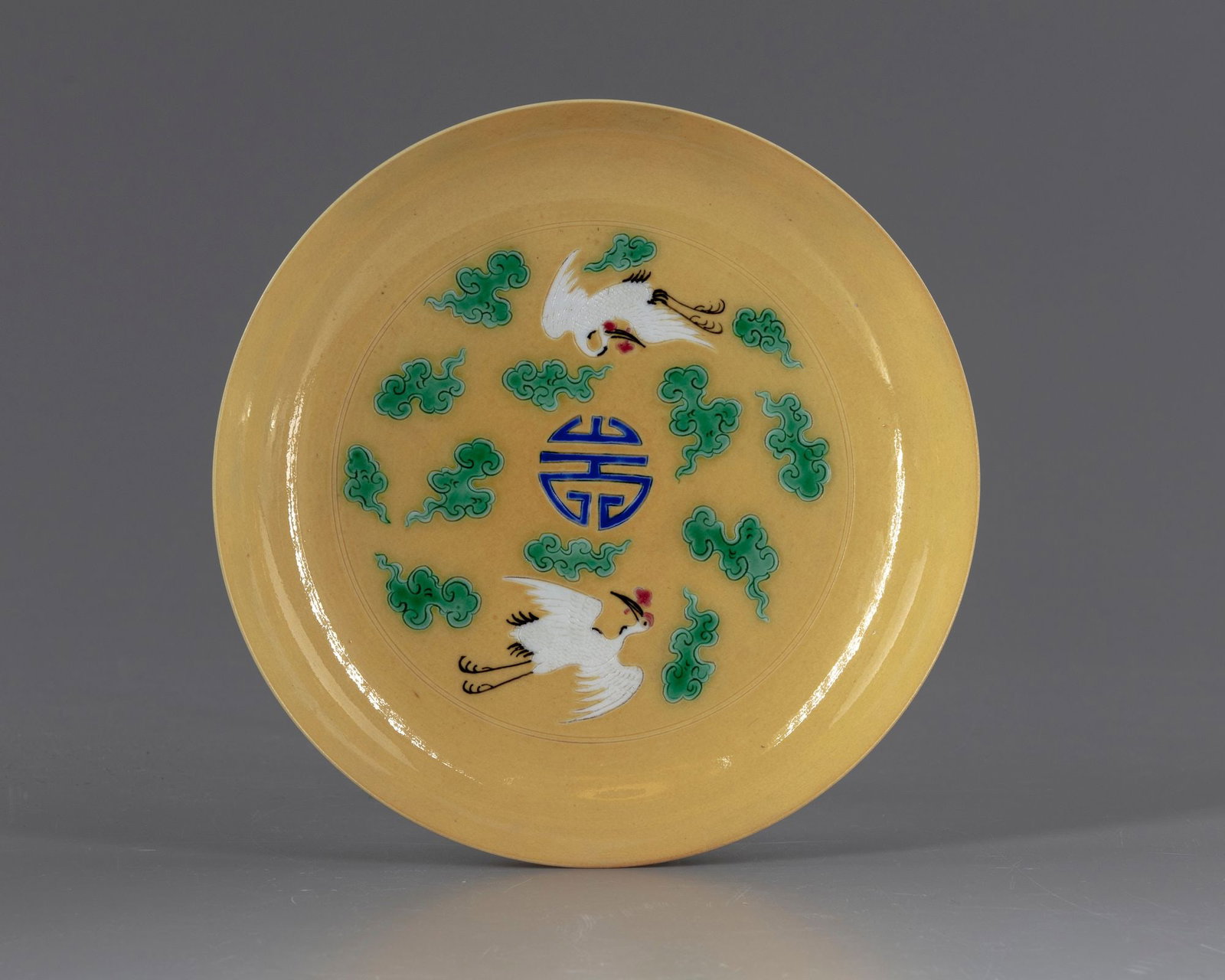 A CHINESE CRANES YELLOW DISH, 20TH CENTURY: A Chinese porcelain dish, decorated to the interior with a shou symbol surrounded by two cranes and clouds, to the exterior with cranes and clouds above waves. The bottom with a Chinese Yongzheng six 