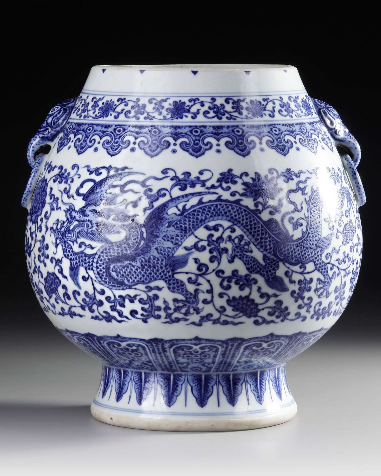 A CHINESE BLUE AND WHITE DRAGON VASE, QING DYNASTY (1644-1911): A Chinese porcelain vase, stylised with two elegant head-shaped handles fitted with rings, decorated in underglaze blue with two five-clawed dragons flying amidst scrolling foliage of lotus and peonie