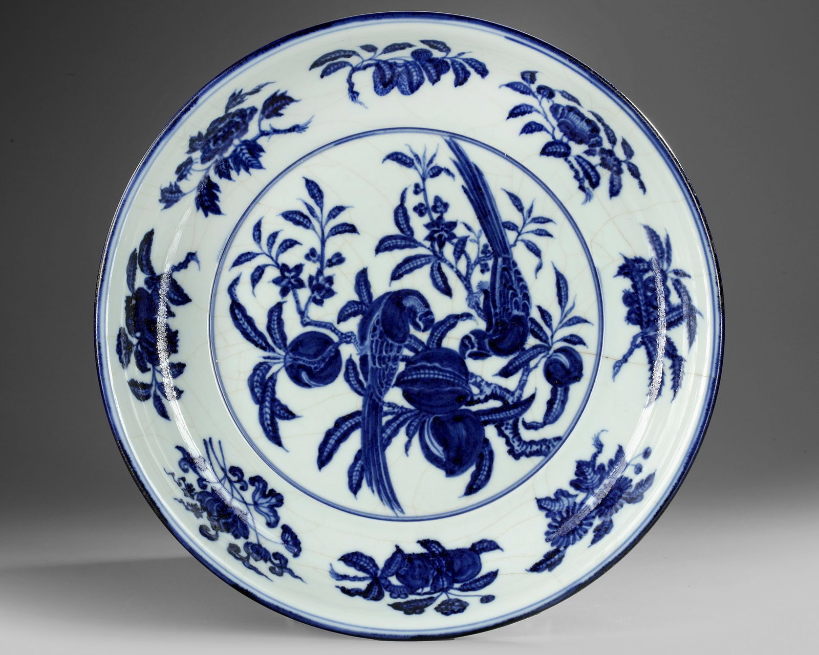 A CHINESE BLUE AND WHITE 'BIRDS' CHARGER, QING DYNASTY (1644â€“1911): A Chinese porcelain blue and white charger with rounded sides and an everted rim, decorated in cobalt blue with an asymmetric 'flower-and-bird' composition depicting two long-tailed birds perched on a