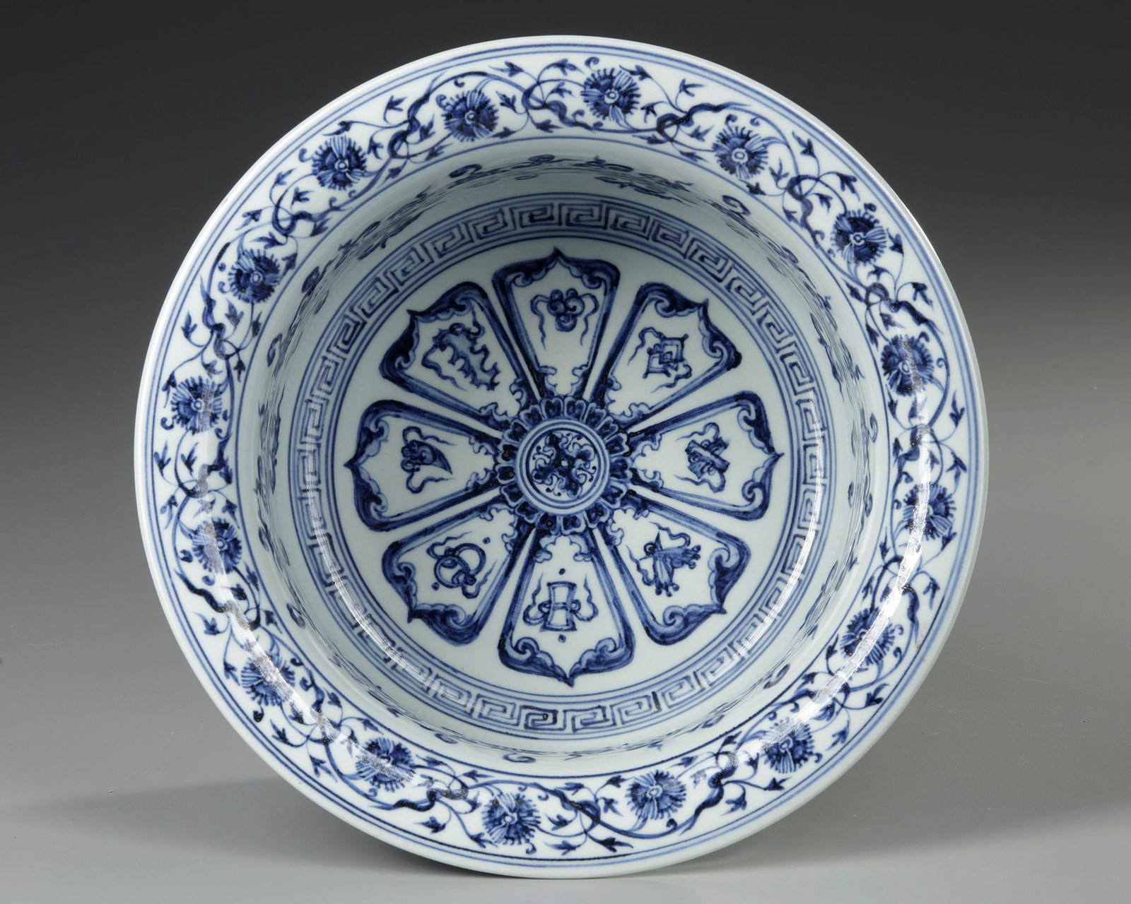A CHINESE BLUE AND WHITE MING-STYLE BASIN, QING DYNASTY (1644-1911): A basin with slightly tapered sides rising to a wide flared rim, the flat interior beautifully and richly painted in cobalt-blue tones, with the more pointed hexafoil rosette, has a rim border of quat