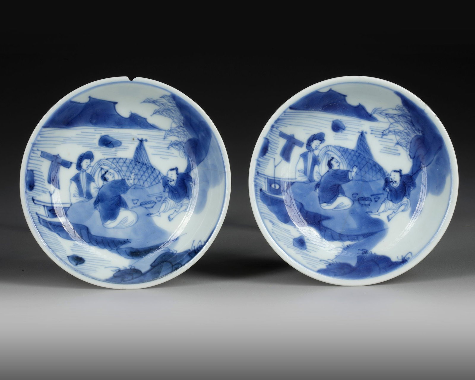A PAIR OF BLUE AND WHITE DISHES, TRANSITIONAL PERIOD, 17TH CENTURY: Decorated in underglaze blue with a river landscape and three figures sitting along the waters edge. Diameter: 11.3 cm. PROVENANCE Private collection, Belgium