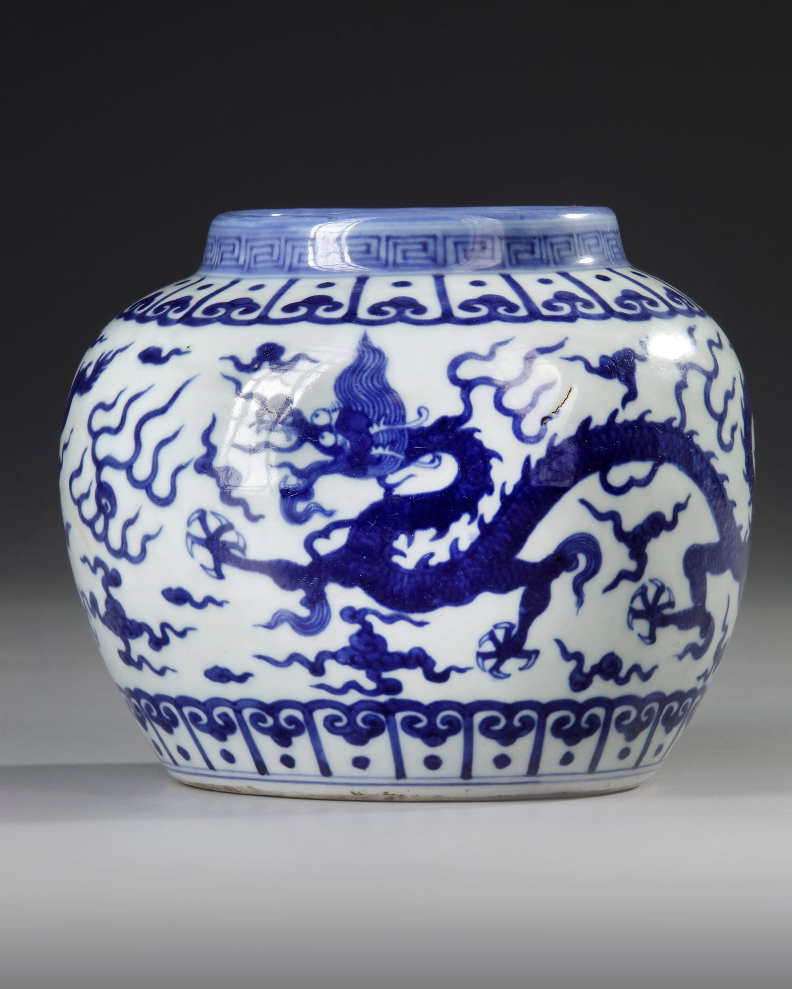 A CHINESE BLUE AND WHITE DRAGONS JAR, MING DYNASTY (1368-1644): A Chinese porcelain jar decorated with five-clawed dragons chasing a flaming pearl amongst clouds, set between a petal lappet border to the shoulder and the base, under a key fret chain to the neck. T