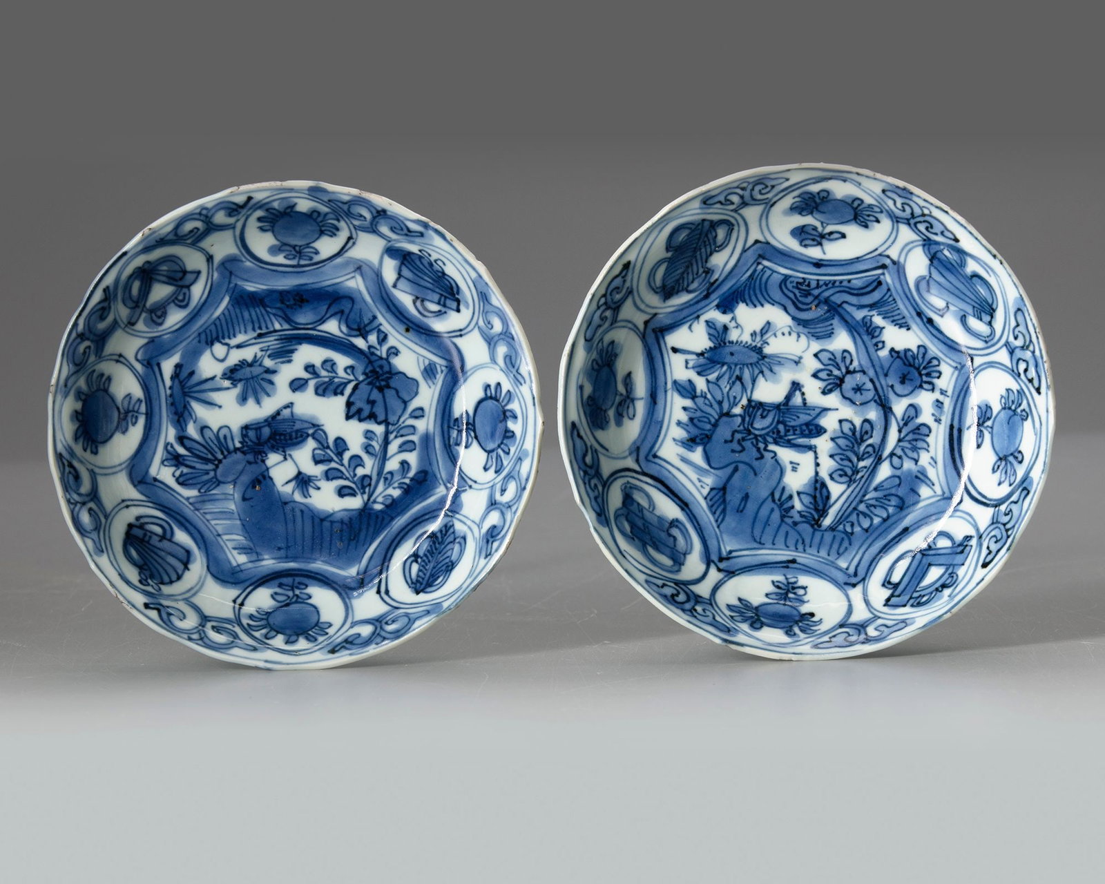 A PAIR OF CHINESE BLUE AND WHITE DISHES, WANLI PERIOD (1572-1620): Each Chinese porcelain dish, finely decorated to the centre with a star-shaped panel enclosing an insect perched on a rock amongst flowers, all surrounded by eight roundels enclosing alternating preci