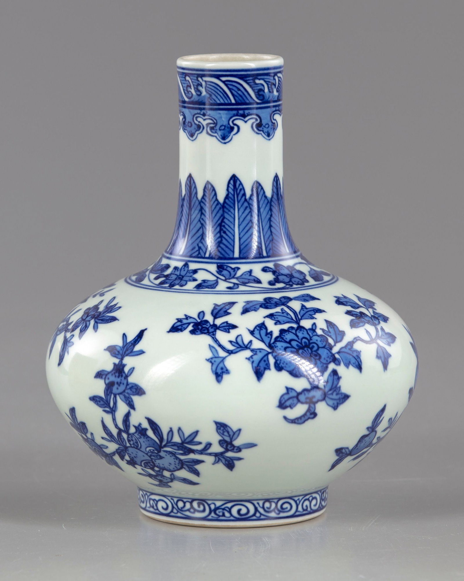 A CHINESE BLUE AND WHITE BOTTLE VASE, 20TH CENTURY: A Chinese blue and white bottle vase, decorated around the body with flower sprays, with fruiting sprays of peach and pomegranate. The neck with upright leaves and a band of ruyi heads. The base with 