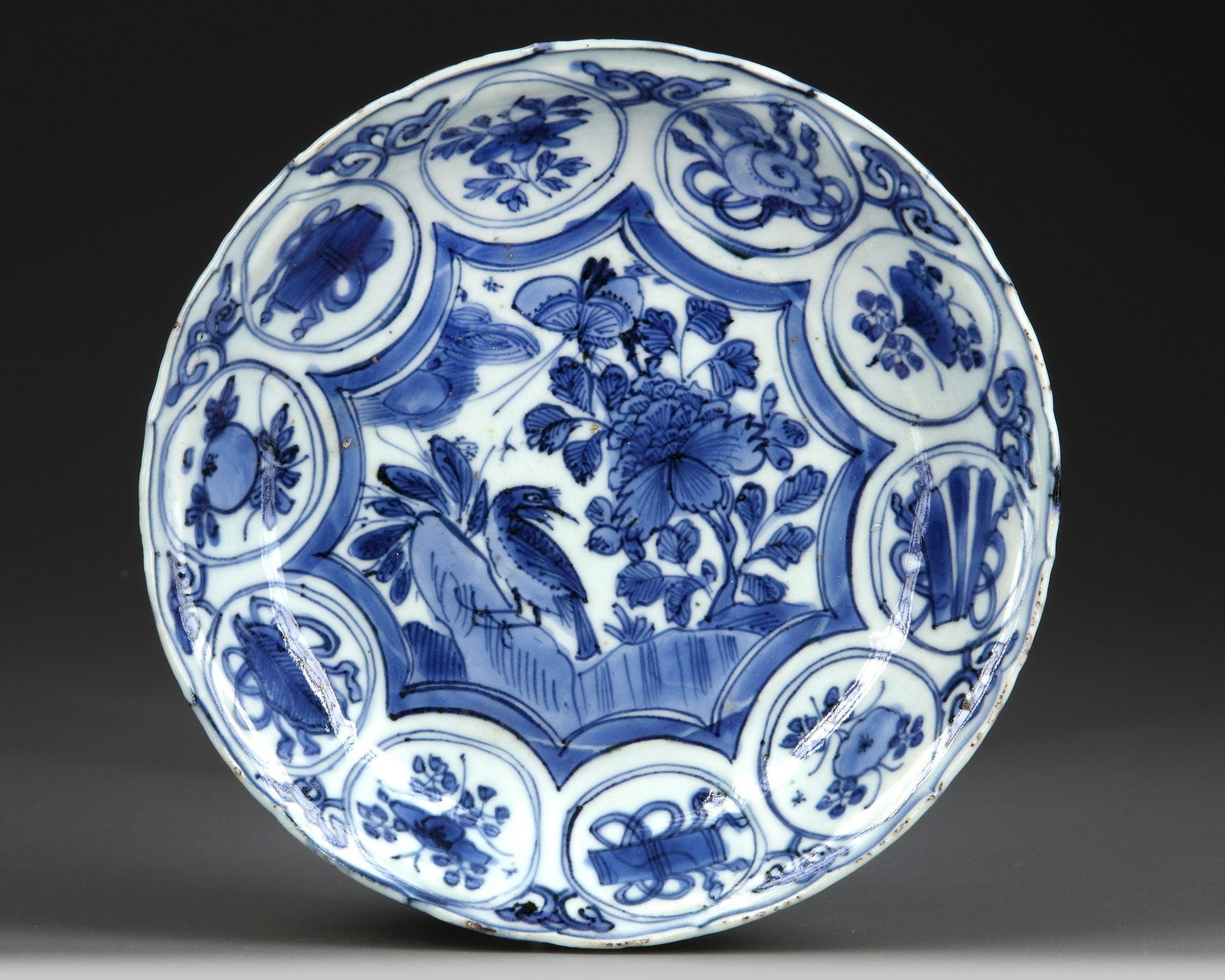 A CHINESE BLUE AND WHITE DISH, WANLI PERIOD (1572-1620): A Chinese porcelain dish, finely decorated to the centre with a star-shaped panel enclosing a bird perched on a rock below a butterfly in flight amongst flowers, all surrounded by eight roundels enclo