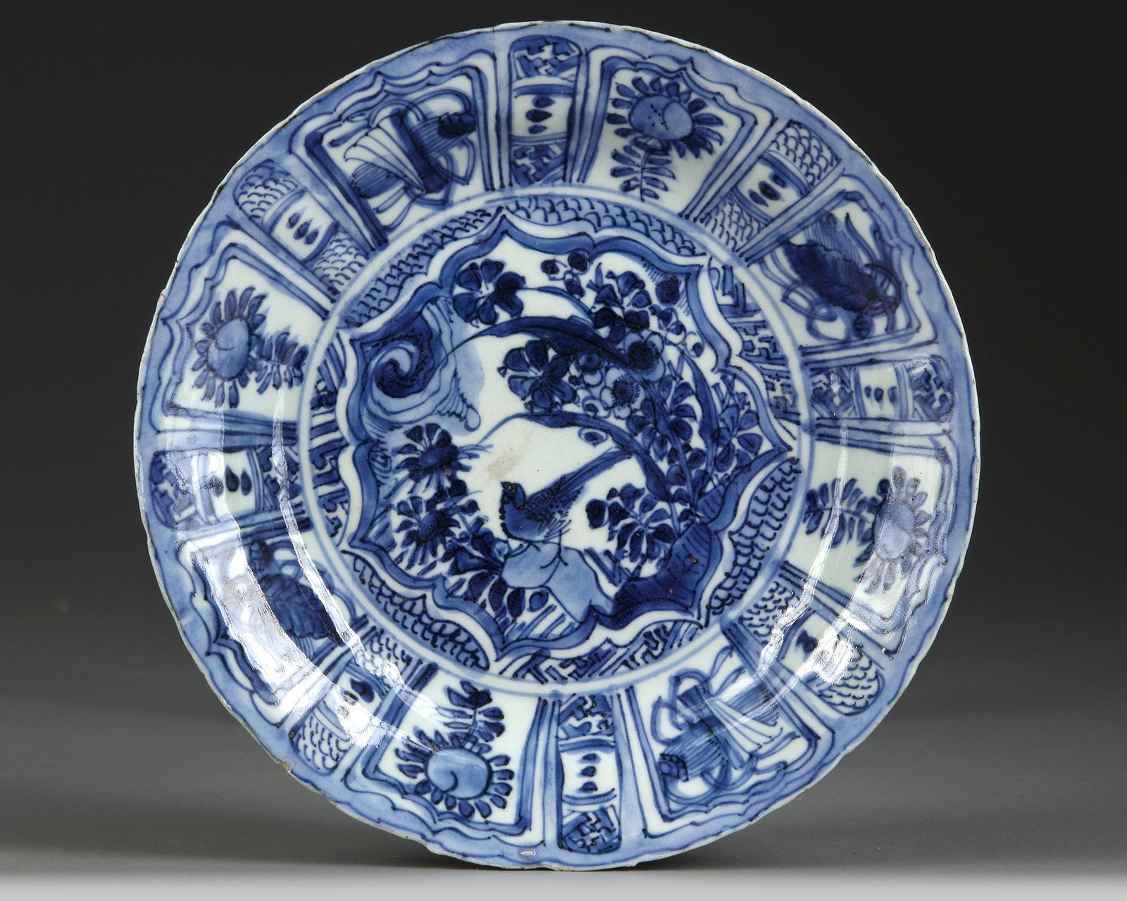 A CHINESE BLUE AND WHITE KRAAK PORCELAIN DISH, WANLI PERIOD (1572-1620): A Chinese porcelain dish, finely decorated to the centre with a star-shaped panel enclosing a bird perched on a rock amongst flowers, all surrounded by further lappet-shaped panels enclosing alternati