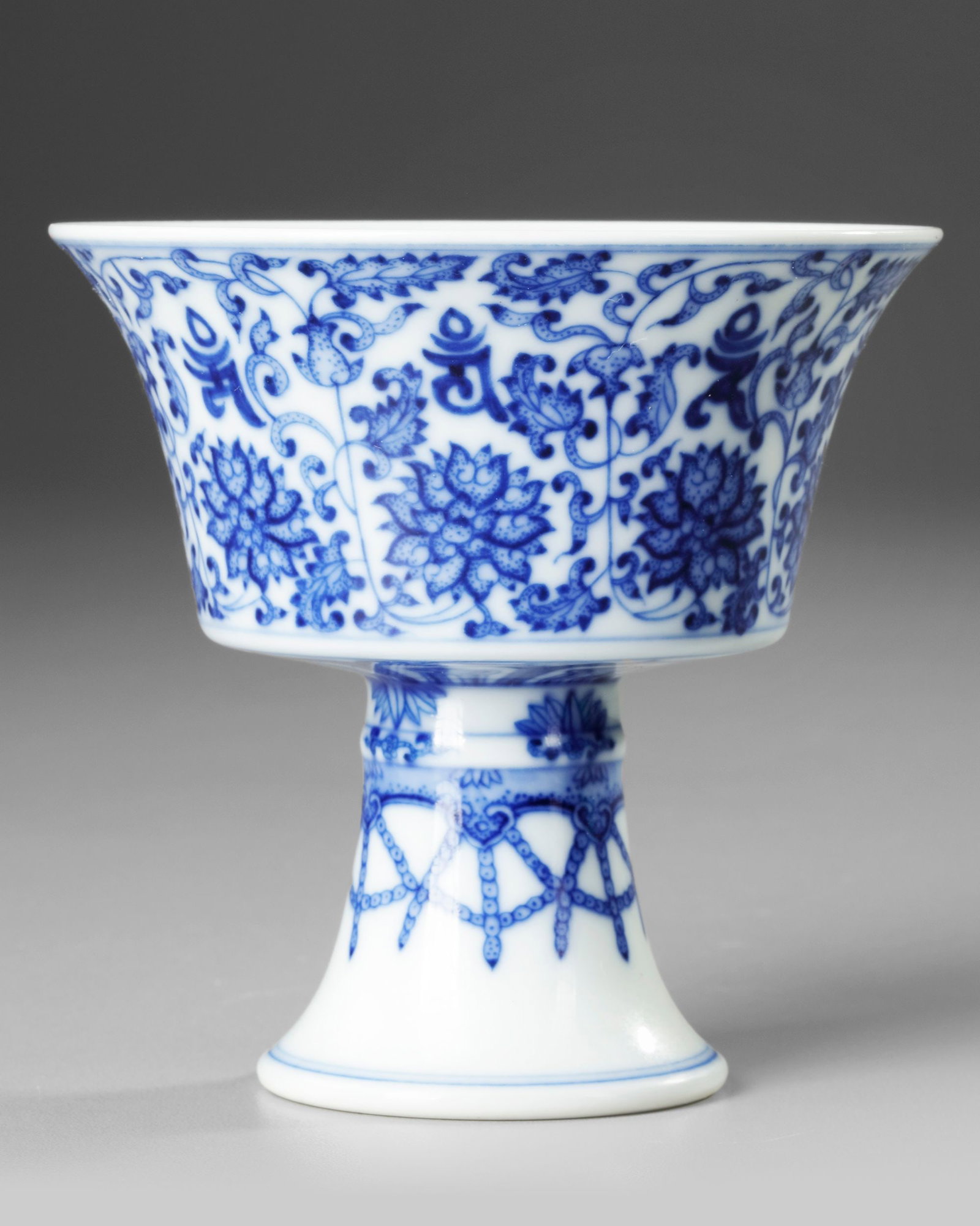 A CHINESE BLUE AND WHITE 'LANCA' STEM CUP, 19TH-20TH CENTURY: Painted around the steep flaring sides with eight lan?§a characters enclosed within undulating lotus stems issuing stylised blossoms and acanthus leaves, the underside with a frieze of tightly-bound 