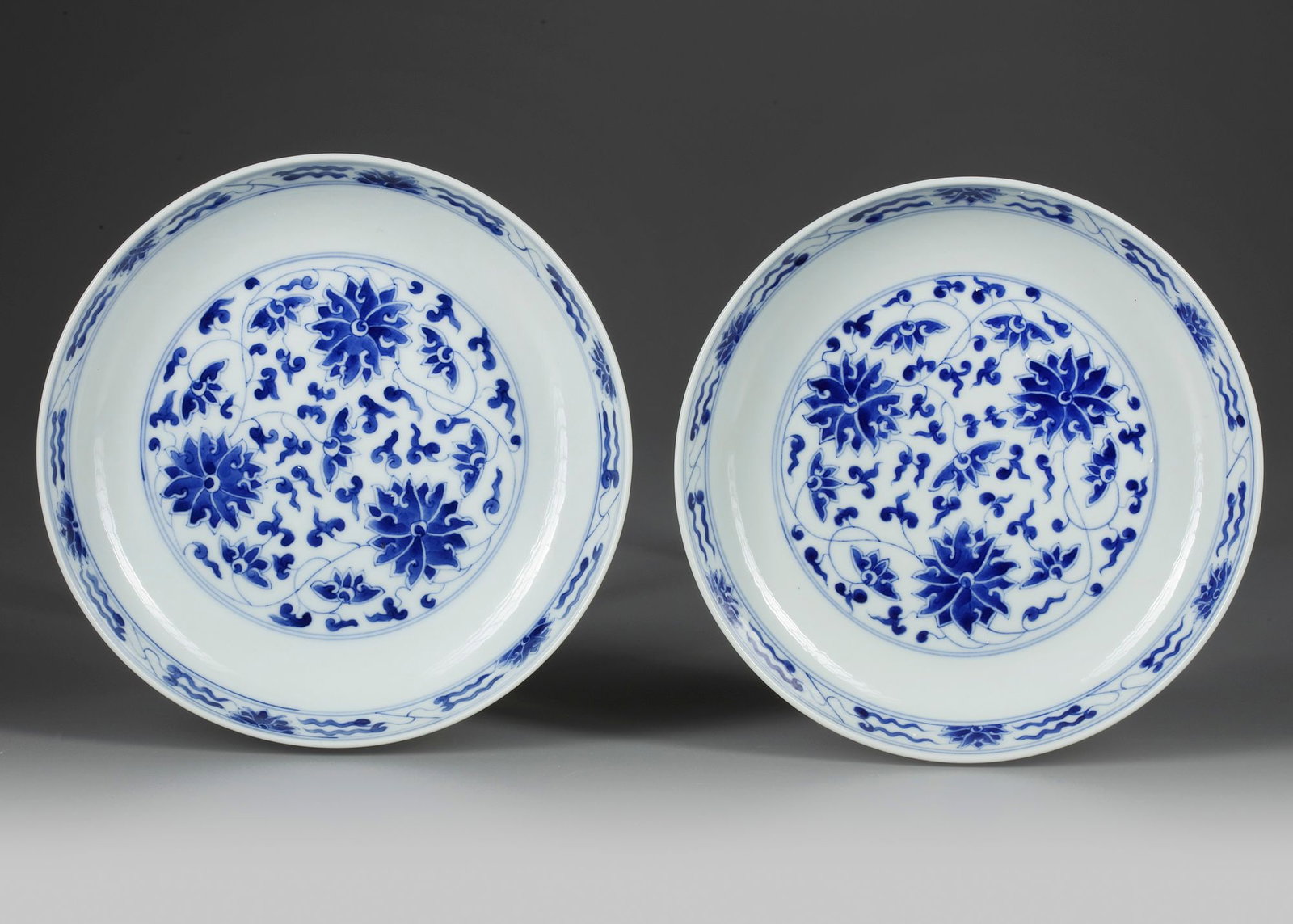 A PAIR OF CHINESE BLUE AND WHITE 'LOTUS' DISHES, 19TH-20TH CENTURY: Each dish is decorated to the centre with a roundel enclosing scrolling lotus, the rims are decorated with a further scroll band. The exterior is similarly decorated, and the bases bear a Guangxu six-
