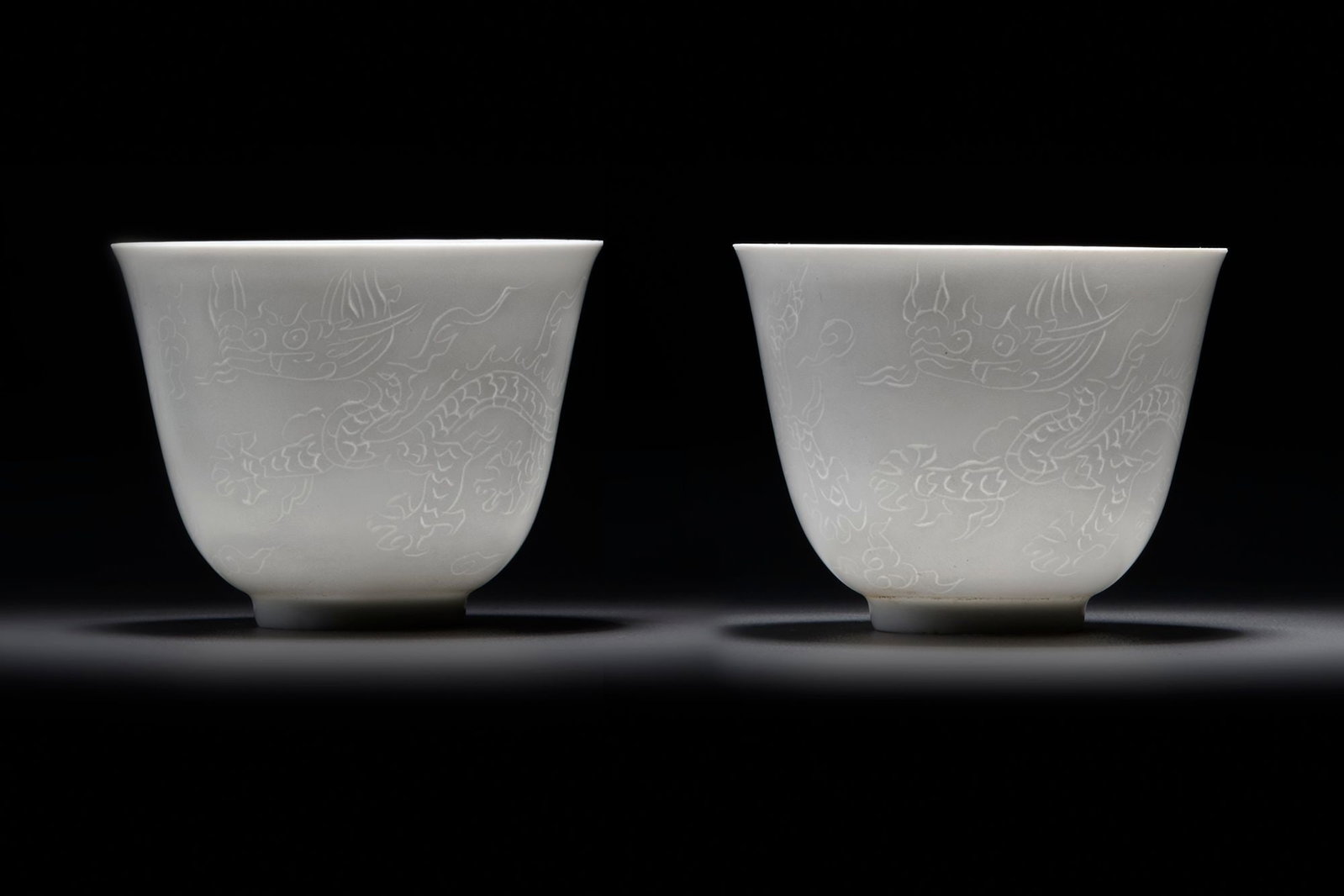 A PAIR OF SMALL CHINESE WHITE-GLAZED DRAGONS CUPS, 20TH CENTURY: Each cup is decorated with two striding anhua dragons above tumultuous waves. The base bears an apocryphal Chenghua mark. Diameter: 6.5 cm. Height: 5.2 cm.