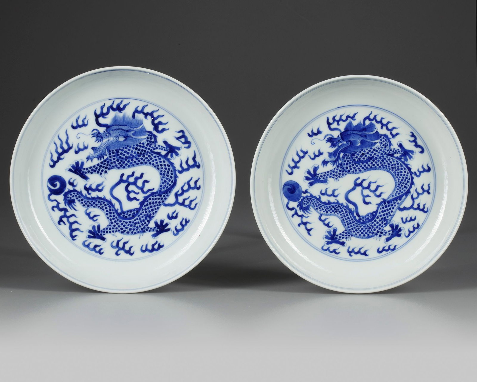 A PAIR OF CHINESE BLUE AND WHITE 'DRAGON' DISHES, 19TH-20TH CENTURY: Each dish is decorated to the centre with a striding dragon chasing the flaming pearl amongst dense flame scrolls. Each reverse is decorated with two further striding dragons and the base with a Guang