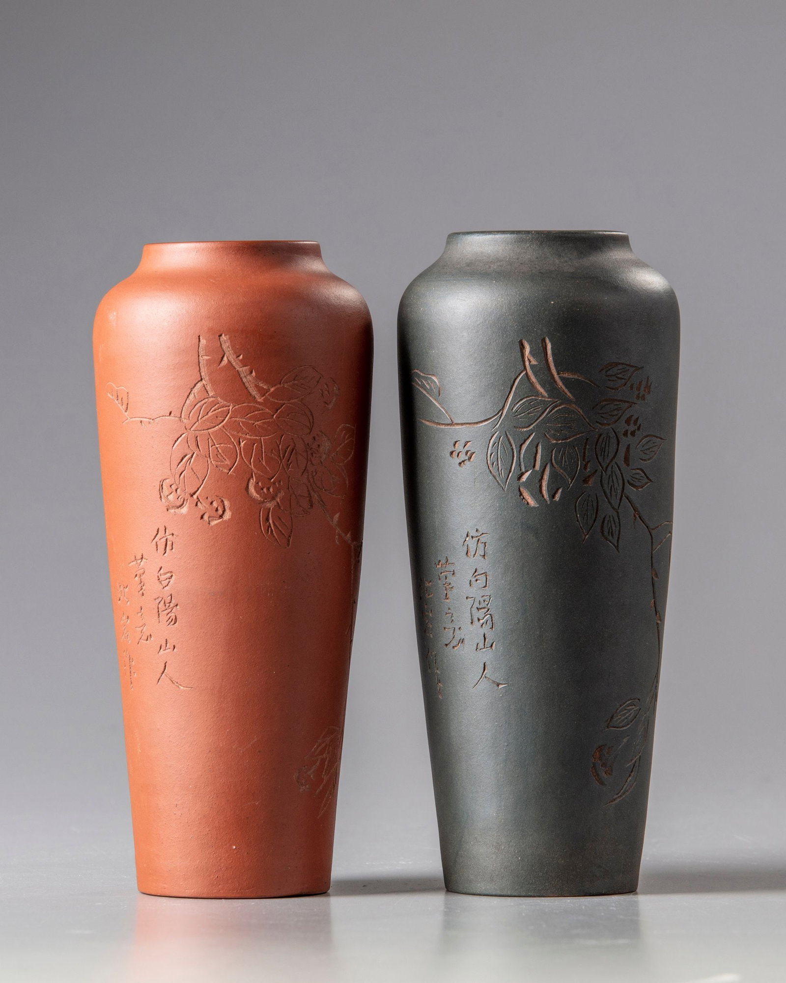A PAIR OF CHINESE YIXING VASES, 19TH CENTURY: The group comprises a red clay vase and a green clay vase, each incised with a leafy branch and an inscription in imitation of 'Bai yang shanren' and signed Bei Yan. Each base is marked with a 'Jindin