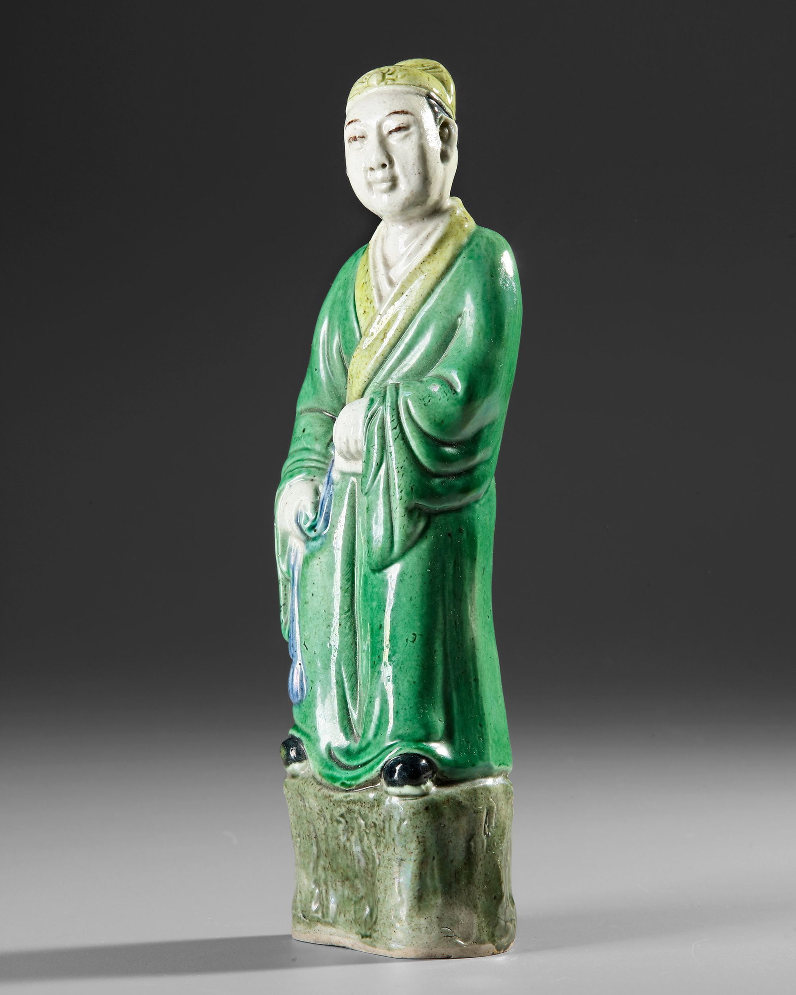 A CHINESE POLYCHROME PORCELAIN FIGURE OF A SCHOLAR, 19TH CENTURY: Elegantly modeled standing figure of a scholar or gentleman in flowing robes, rendered in luminous green, white, yellow, and blue glazes. The serene face and graceful pose convey an air of quiet refin