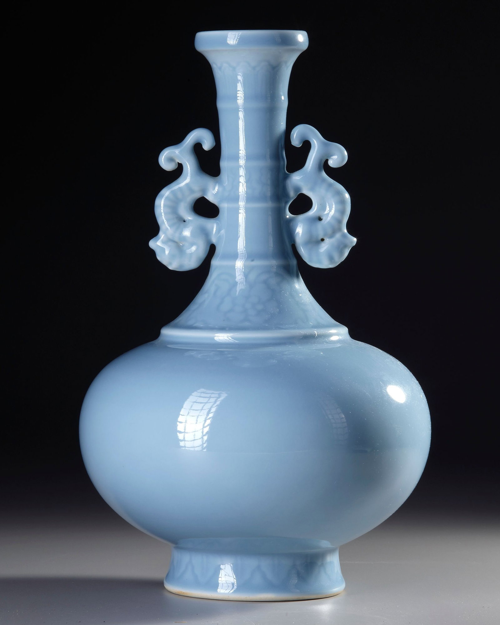 A CHINESE CLAIR-DE-LUNE-GLAZED BOTTLE VASE, 19TH-20TH CENTURY: A Chinese porcelain bottle vase, featuring a compressed globular body rising to a bamboo-moulded neck and adorned with chilong-shaped handles. The exterior is covered in a pale blue, semi-translucent 