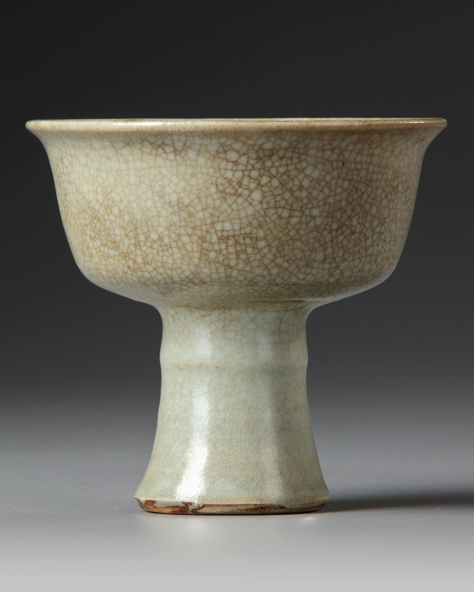 A CHINESE GU-TYPE CRACKLE GLAZED STEMCUP, QING DYNASTY (1644-1911): Supported on a splayed hollow stem foot angled to the cup with steep sides rising from a flat base to a flared mouthrim, covered overall in a caramel brown glaze suffused with dark grey and brown crac