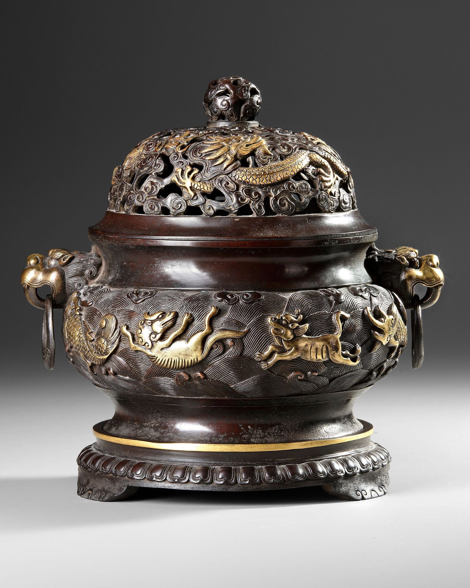 A CHINESE PARCEL-GILT BRONZE 'SEA CREATURES' CENSER, COVER AND STAND: The censer is of bombe form cast with two loose-ring beast-head handles, the body is cast in relief with eight mythical sea creatures picked out in gilt all on a ground of tumultuous waves. The base o