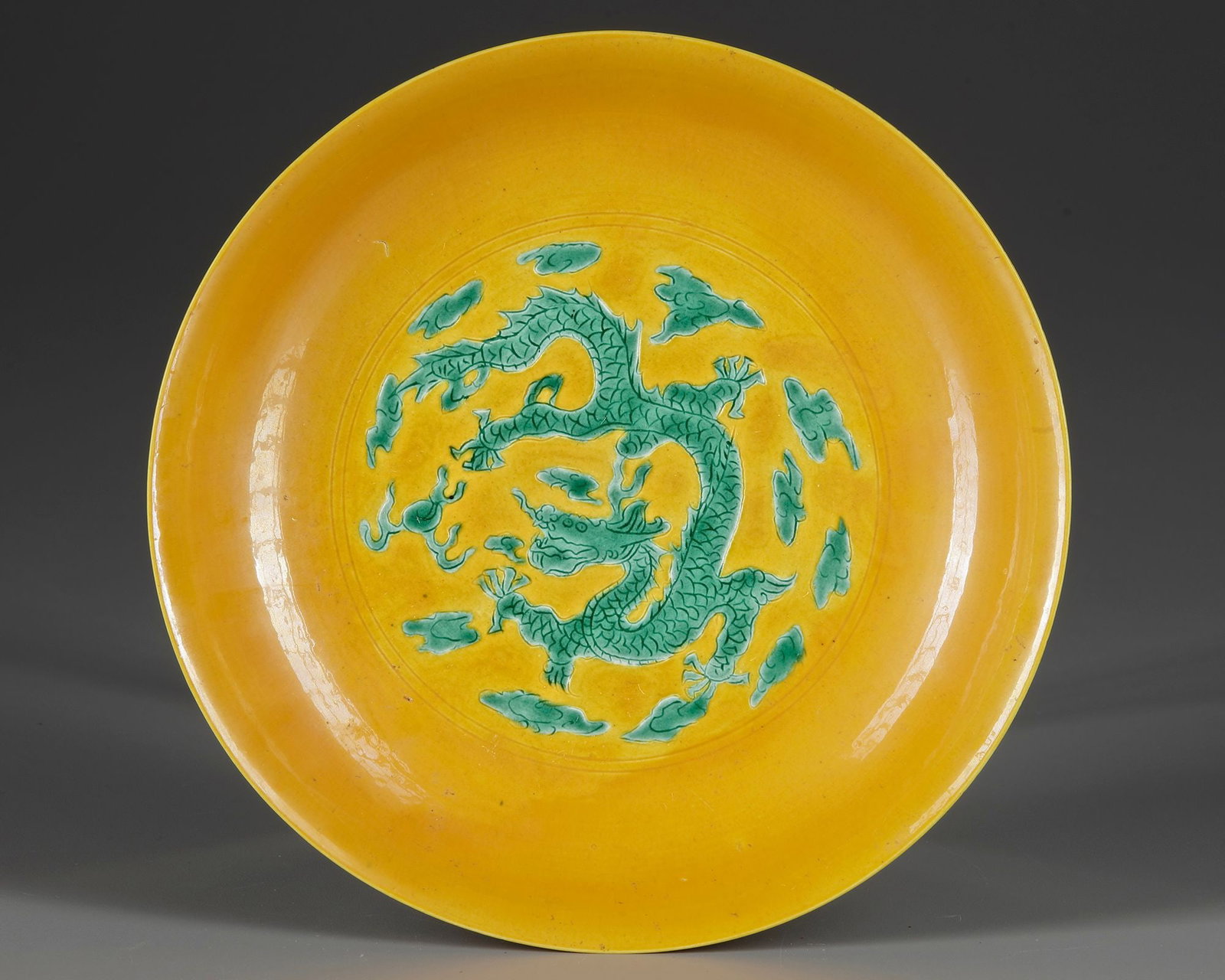 A CHINESE YELLOW-GROUND GREEN-ENAMELLED 'DRAGON' SAUCER,QING DYNASTY (1644â€“1911): A Chinese porcelain dish with rounded sides supported on a short foot. The interior is decorated with a green five-clawed dragon chasing a flaming pearl amidst clouds. The exterior is decorated with a