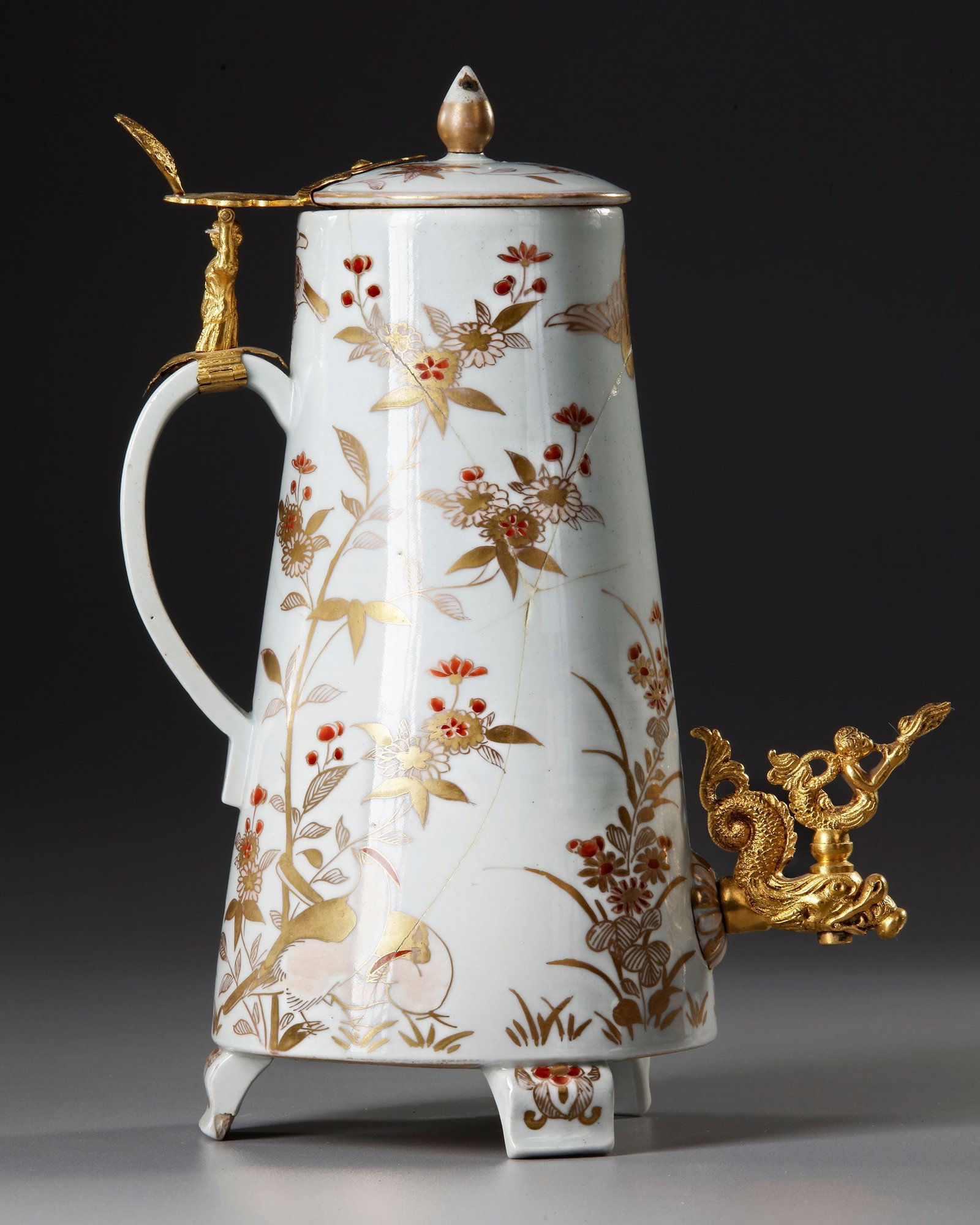 A JAPANESE IMARI PORCELAIN COFFEE POT AND COVER, EDO PERIOD (1603-1868): The conical body raised on three feet, with applied C-shaped handle and cover with knob finial, painted in overglaze gold and iron-red enamels with birds and flowers. Height 30 cm. Repaired.