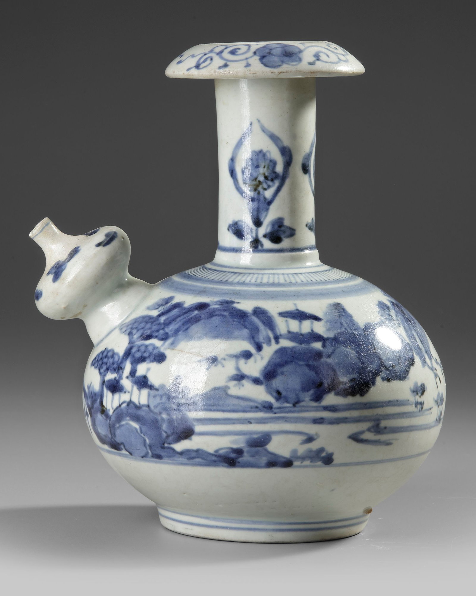 A JAPANESE BLUE AND WHITE ARITA KENDI, 17TH CENTURY: Kendi on footring, a bulbous spout on the shoulder , cylindrical neck ending in a splayed mouth with overturned rim. Decorated in underglaze blue with a simplified landscape, the shoulder and the rim 
