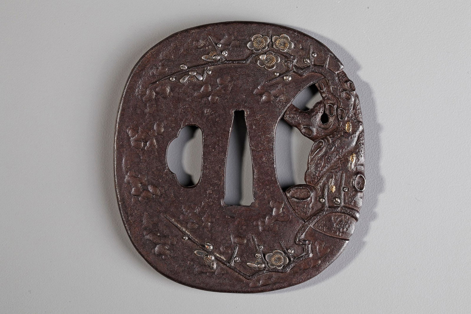 A JAPANESE TSUBA,EDO PERIOD (1615â€“1868): Of rounded rectangular form, carved and pierced in relief of a plum tree, inlaid with gold and silver. Diameter .7.8 cm.