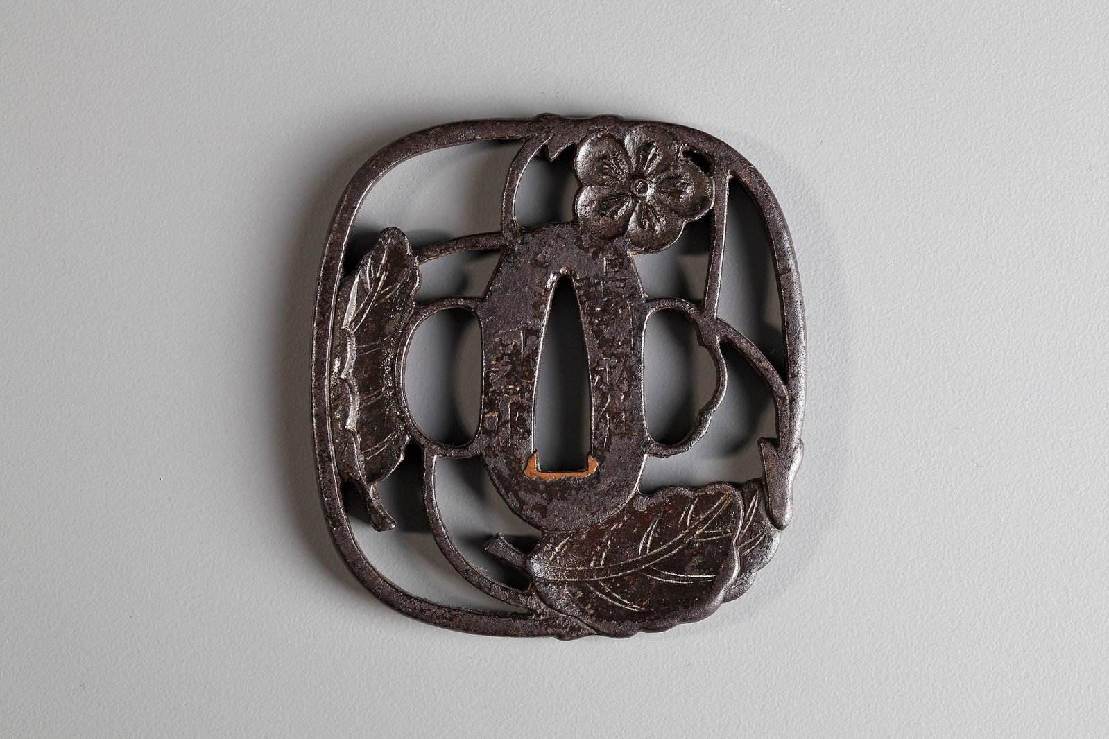 A JAPANESE TSUBA,EDO PERIOD (1615â€“1868): Of rounded rectangular shape, carved and pierced with a two leaves and a blossom, signed. 6.7 by 7 cm.