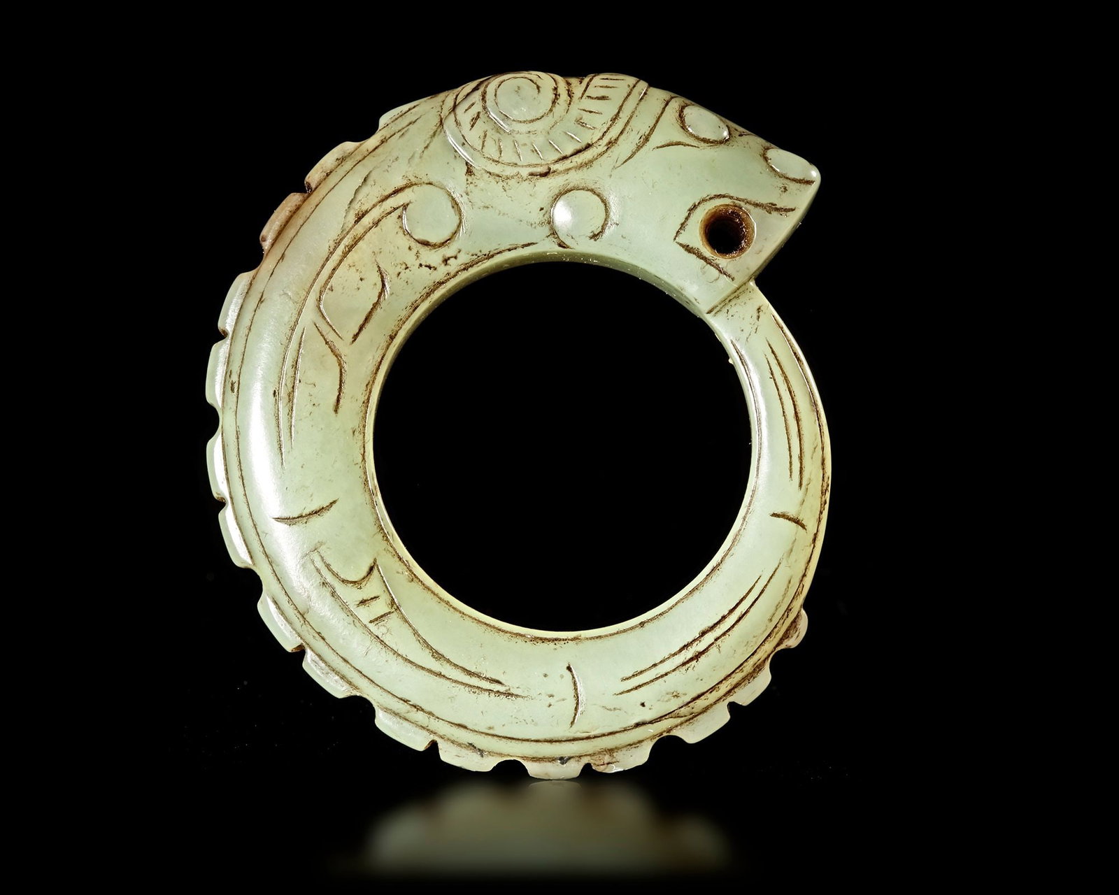 A LIGHT GREEN JADE OUROBOROS DRAGON PENDANT, CHINA, WESTERN ZHOU DYNASTY: 6 cm. PROVENANCE Purchased in 1996 from Mr. Frank H. Crane, a Canadian antique dealer. His shop, "The Hundred Antiques" was located in Stirling, Ontario, Canada.