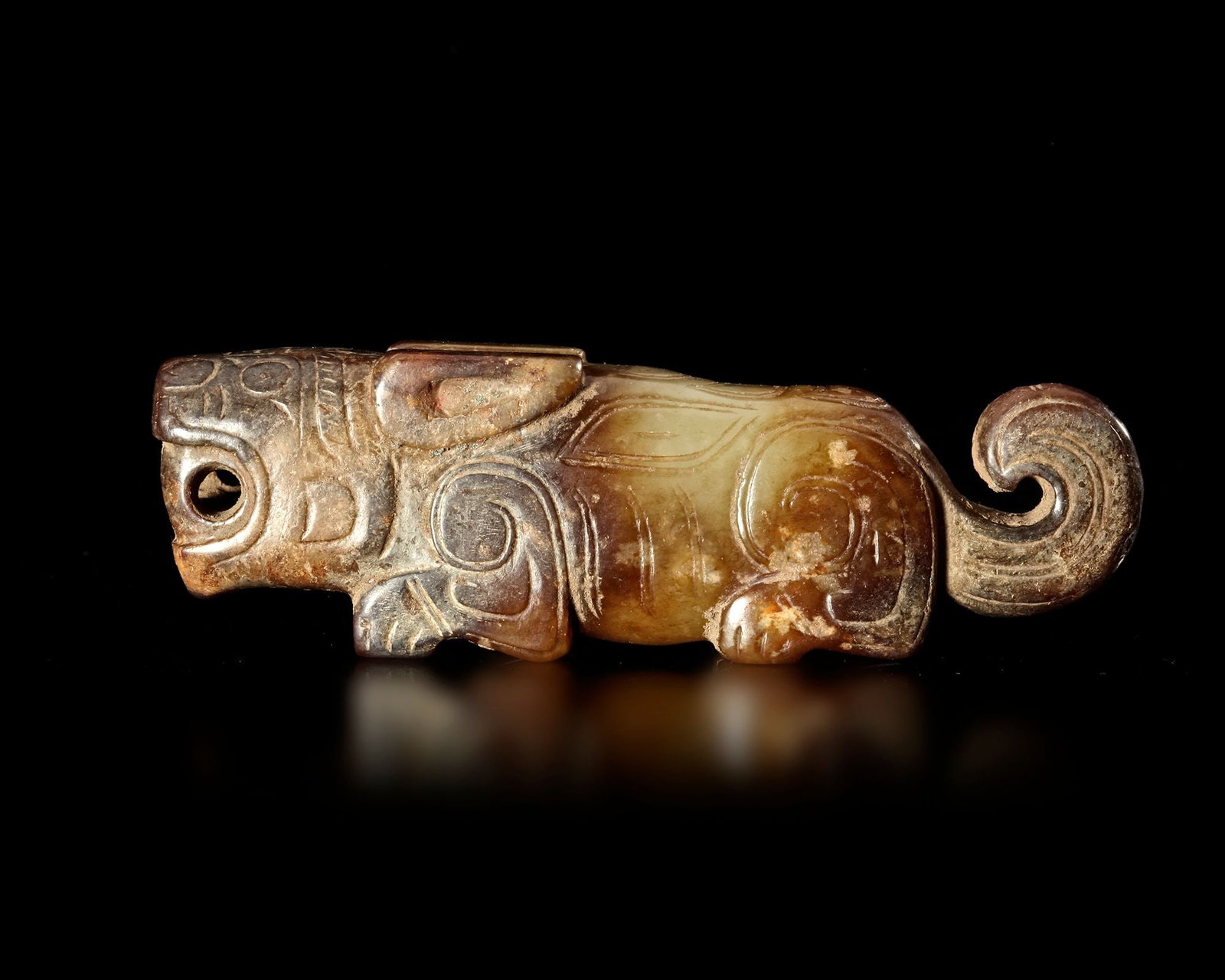 A JADE OF A RECUMBENT TIGER WITH ITS TAIL CURLED UPWARD, CHINA, SHANG DYNASTY: Decorated with stylized markings on the body. Length 10,3 cm. PROVENANCE Purchased in 1996 from Mr. Frank H. Crane, a Canadian antique dealer. His shop, "The Hundred Antiques" was located in Stirling,