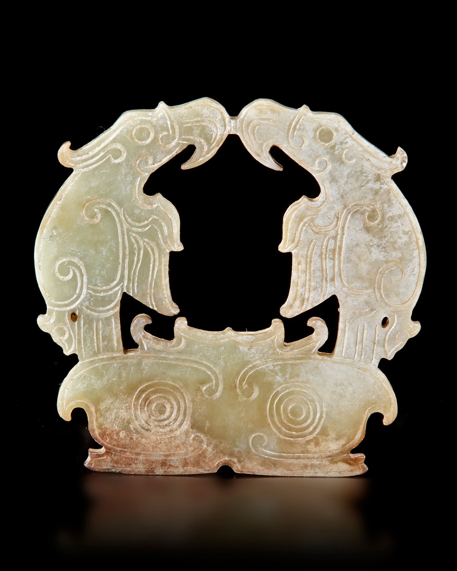 A CHINESE GREEN JADE TWIN-EAGLE PLAQUE, POST-SHIJIAHE CULTURE (CIRCA 2000â€“1800 BC): A finely carved green jade plaque depicting two stylized eagles facing one another in a symmetrical composition. The elegant openwork design and flowing spiral motifs reflect the sophisticated artisti