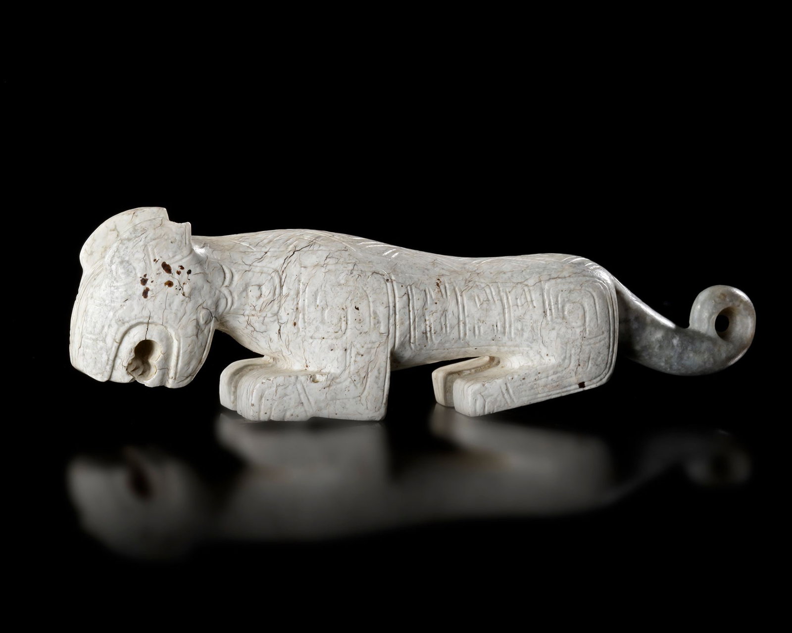 A CHINESE WHITE JADE TIGER, SHANG DYNASTY (CIRCA 1600â€“1046 BC): A rare white jade tiger carved in a powerful recumbent pose, embodying strength, courage, and protection. Finely incised geometric and stylized motifs decorate the body. The sculpture displays a smoot