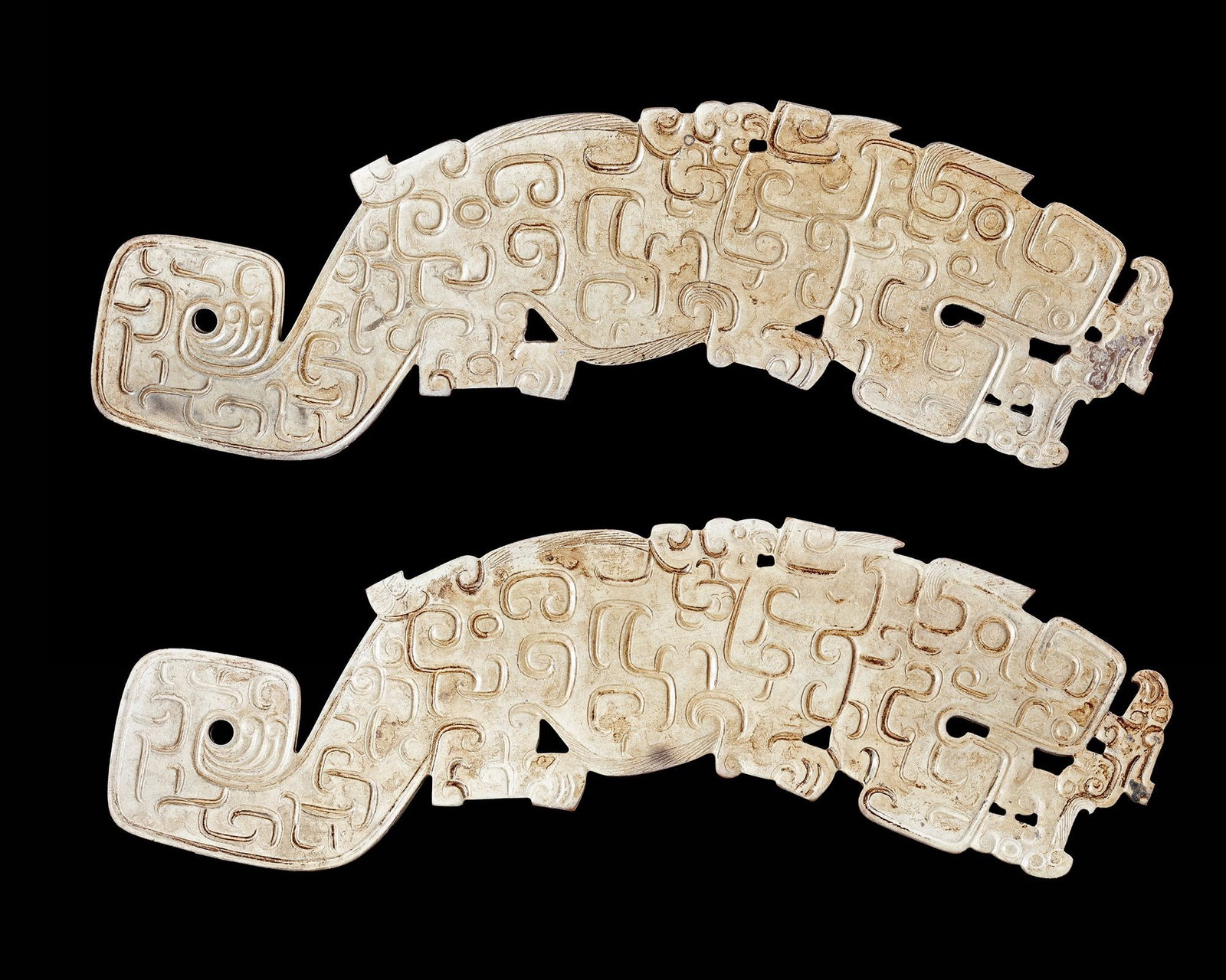 A PAIR OF WHITE LARGE JADE TIGERS, CHINA, SPRING AND AUTUMN PERIOD (770â€“476 BC): An exceptional pair of creamy white jade tiger plaques from the Spring and Autumn period, each finely carved with intricate scroll motifs and surmounted by a stylized bird. The dynamic composition com
