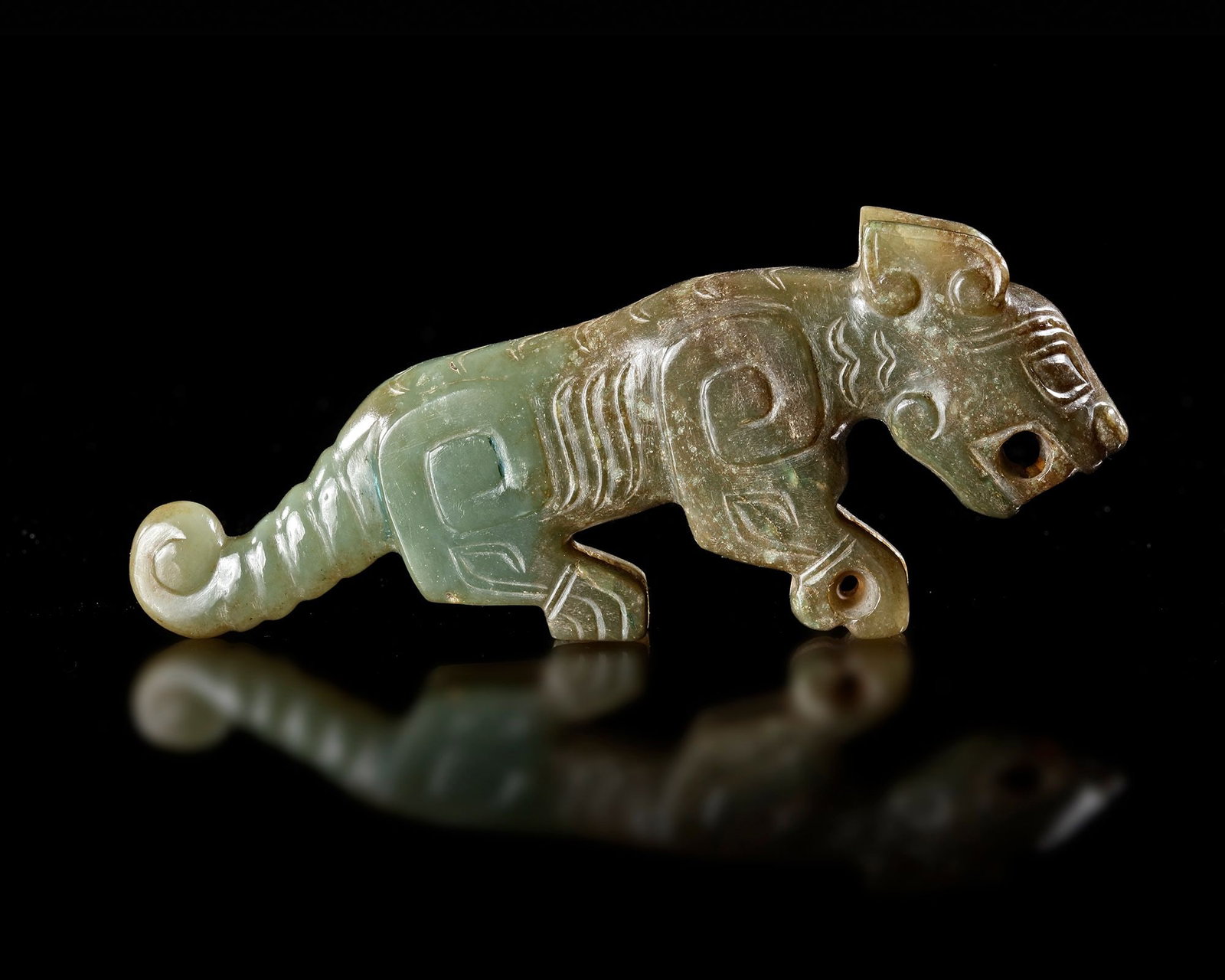A JADE TIGER, CHINA, SHANG DYNASTY (CIRCA 1600â€“1046 BC): A finely carved green jade tiger displaying the powerful and stylized forms characteristic of early Chinese ritual art. Decorated with geometric motifs and a curled tail, the figure embodies strength,