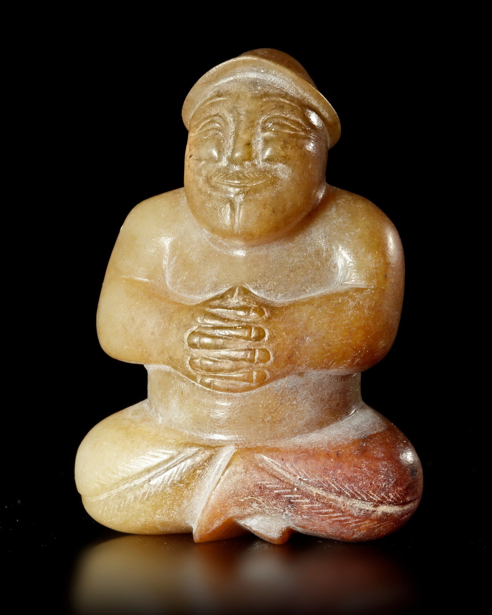 A BEIGE BROWN JADE CROSS LEGGED MALE FIGURE, CHINA, EASTER HAN DYNASTY (25 AD-220 AD): With hands held together in front of his chest. His face carved with a wide smile. 5,3 cm. PROVENANCE Purchased in 1996 from Mr. Frank H. Crane, a Canadian antique dealer. His shop, "The Hundred Antiq