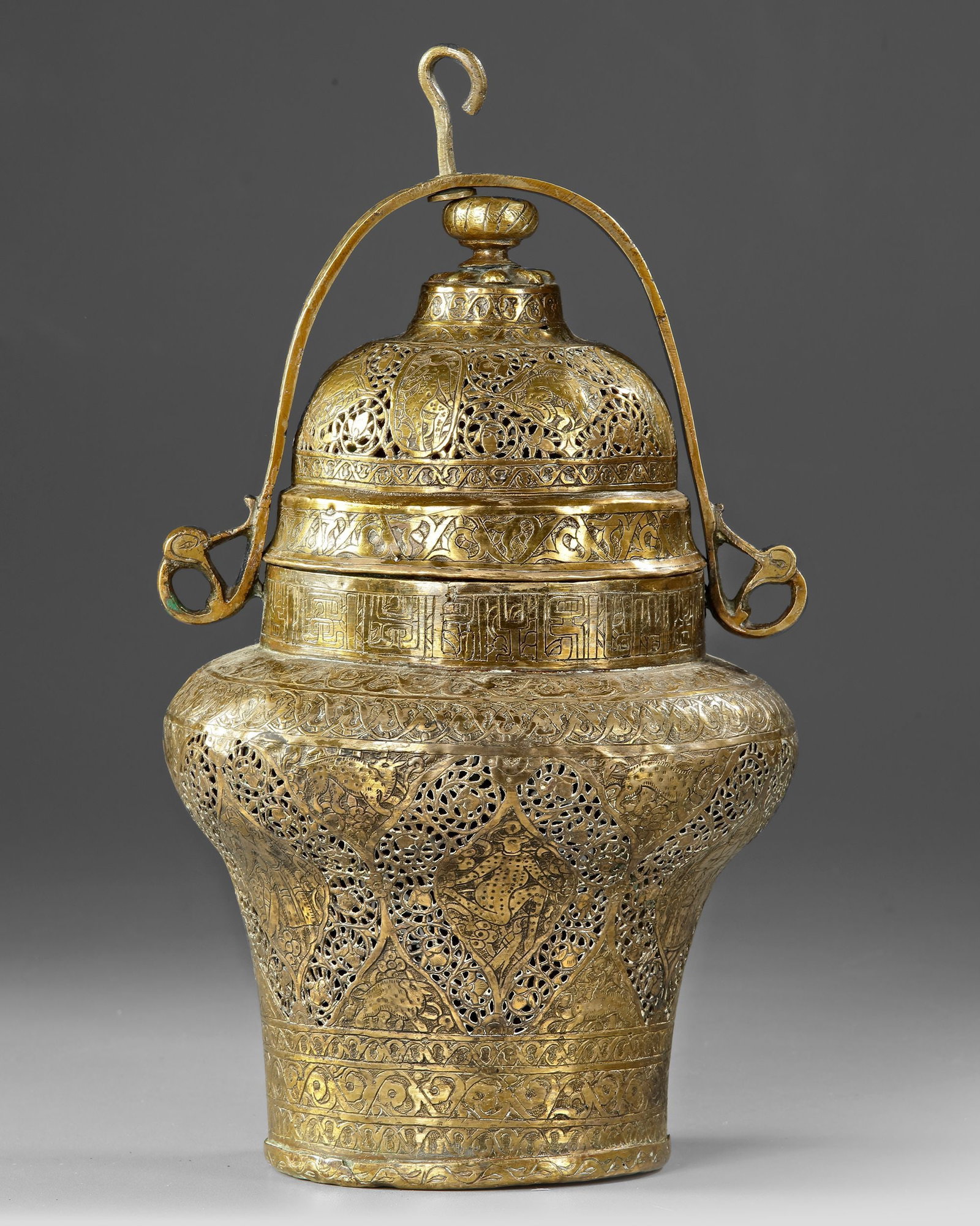 A QAJAR PERSIAN GILT BRONZE INCENSE BURNER, PERSIA 19TH CENTURY: A gilt bronze incense burner in the form of an oil holder, decorated with panels featuring engraved animals, mythical beasts, and standing figures on a pieced floral ground. Height: 25 cm.
