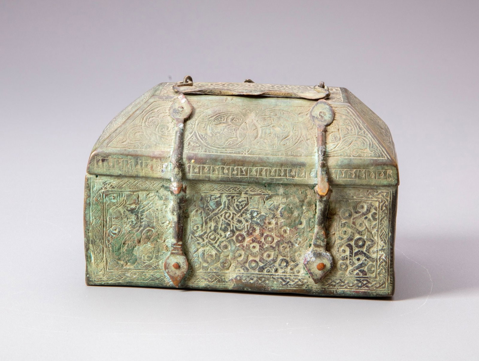 A KHORASAN PERSIAN BRONZE CASKET, PERSIA 12TH/13TH CENTURY: Rectangular bronze casket with a gently domed, hinged lid, the exterior extensively decorated with finely engraved arabesques, scrolling foliage and interlacing geometric motifs within framed panels. 