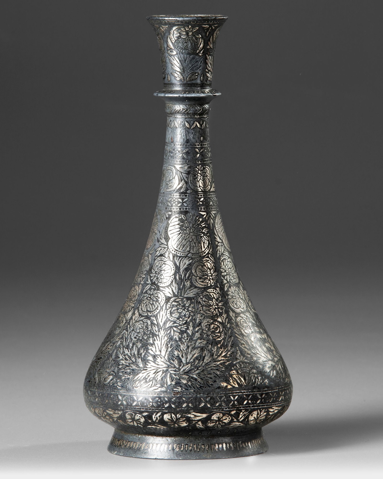 A SILVER INLAID BIDRI VASE, INDIA 19TH CENTURY: A silver inlaid vase, elegantly raised on a rounded pedestal foot, features a teardrop-shaped body and a narrowing neck with a wide, flat, rounded collar. The body is adorned with a dense design of fl