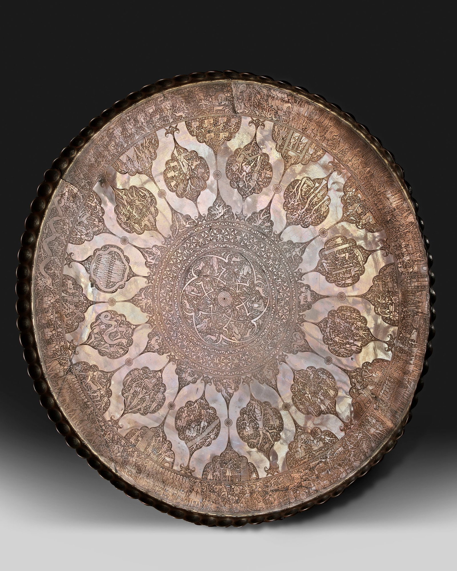 A LARGE PERSIAN BRONZE TRAY, ZAND DYNASTY,1800: A Persian circular bronze tray intricately engraved with scenes from Persian mythology. The center of the tray often depicts cosmic battles, such as Ahura Mazda, the god of light, in his struggle agai