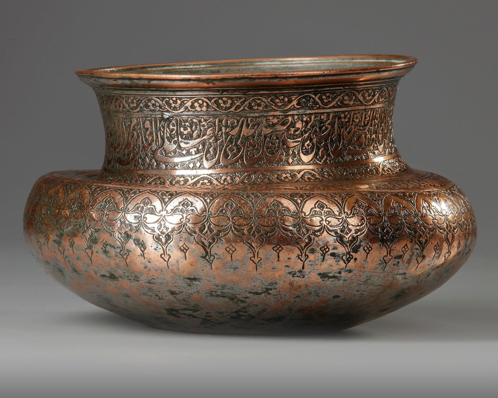 A LATE SAFAVID TINNED COPPER BOWL, PERSIA, 18TH CENTURY: Of wide rounded form on rounded base, the waisted neck with everted mouth, the shoulder with a band of interlaced floral scroll, the neck engraved with a register of dense nasta'liq calligraphy agains