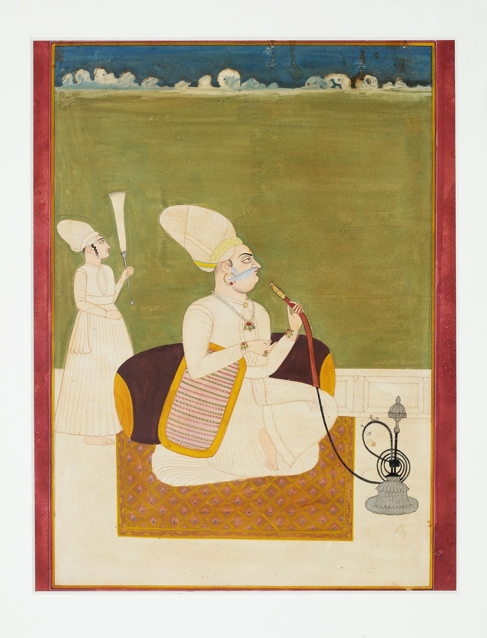 A PRINCE SMOKING A HOOKAH, NORTH INDIA,19TH CENTURY: Gouache heightened with gold and silver on paper, a ruler, seated on a terrace, smoking a hooka, an attendant waving a morchal above him, applied red surround with orange and white rules. 39 by 29 cm.