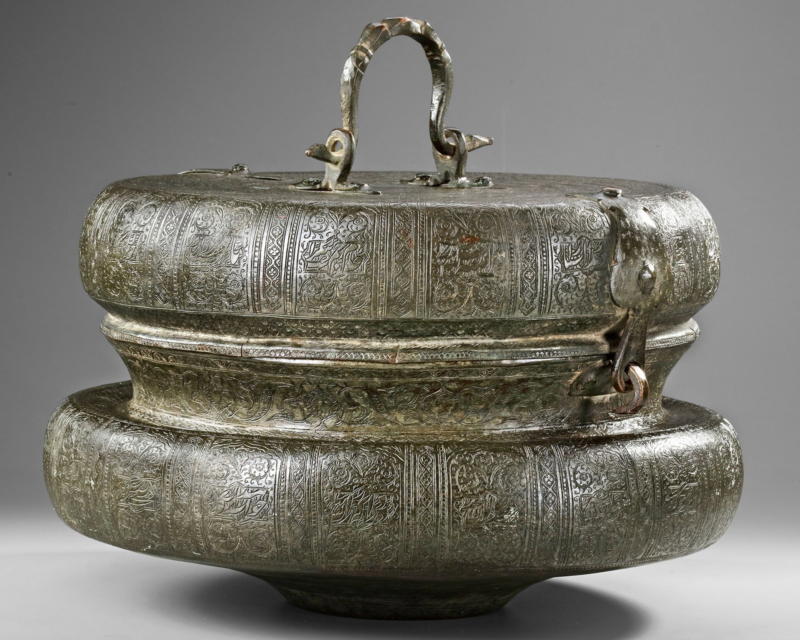A SAFAVID TINNED COPPER BOWL AND COVER, PERSIA, 17TH CENTURY: A large tinned copper bowl with compressed rounded body, With a handle. The body and lid engraved with bands enclosing interlacing flowers and split-palmettes against a hatched ground. The rim with a 