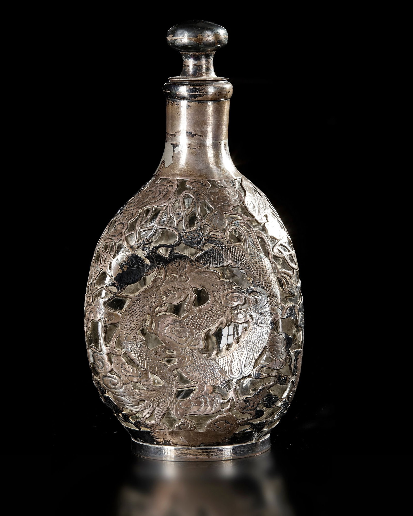 A CHINESE SILVER-OVERLAID GLASS BOTTLE, 19TH CENTURY: A Chinese glass bottle of elegant baluster form, lavishly decorated with finely worked silver overlay depicting dragons among scrolling clouds. The mythical creatures are rendered in relief with detai
