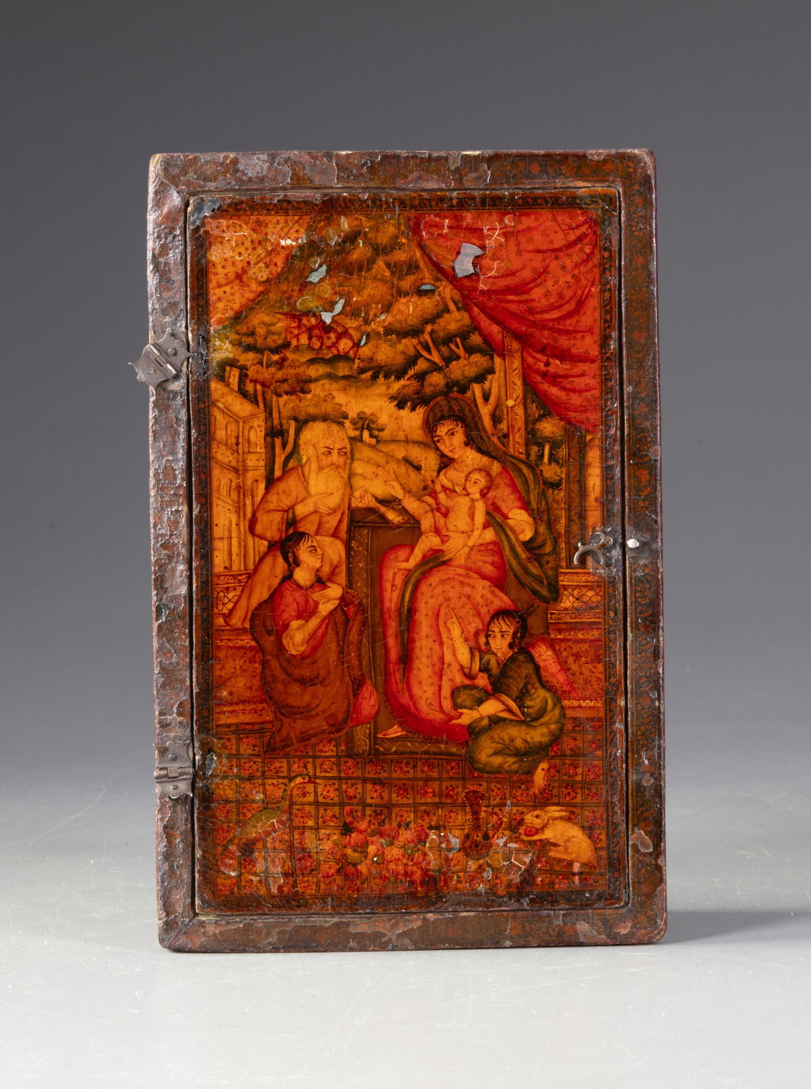 A QAJAR MIRROR, EARLY 19TH CENTURY: A rare Qajar-period mirror housed in a lacquered case, finely painted with figural scenes in warm tones of red, gold, and brown. The decoration depicts elegant courtly figures within a landscaped sett