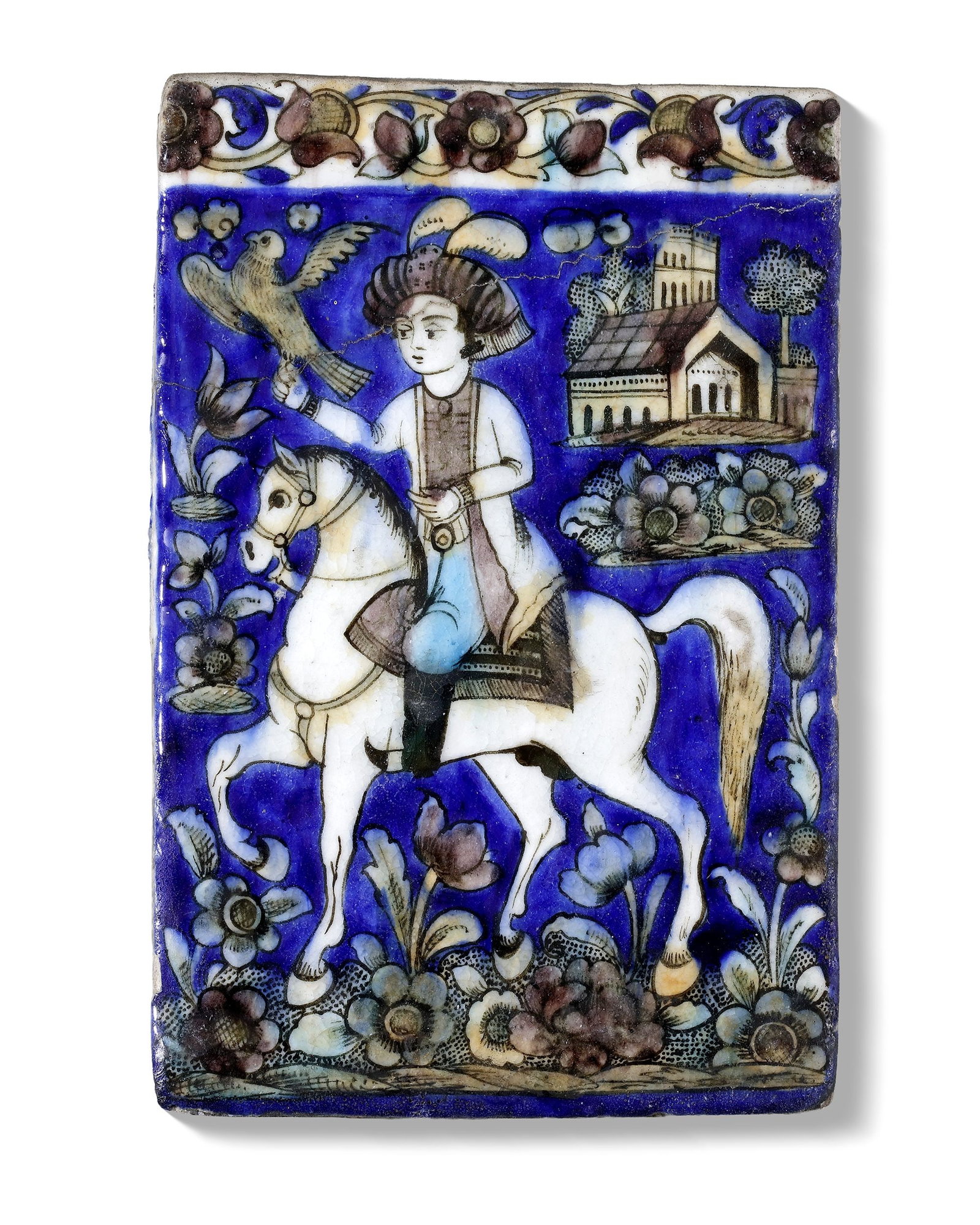 A POLYCHROME MOULDED POTTERY TILE, PERSIA QAJAR, 19TH CENTURY: A finely painted Qajar Persian tile, decorated in underglaze blue, turquoise, and green, depicting a youthful falconer riding a white horse within a stylized landscape. Set against a rich cobalt-blue 